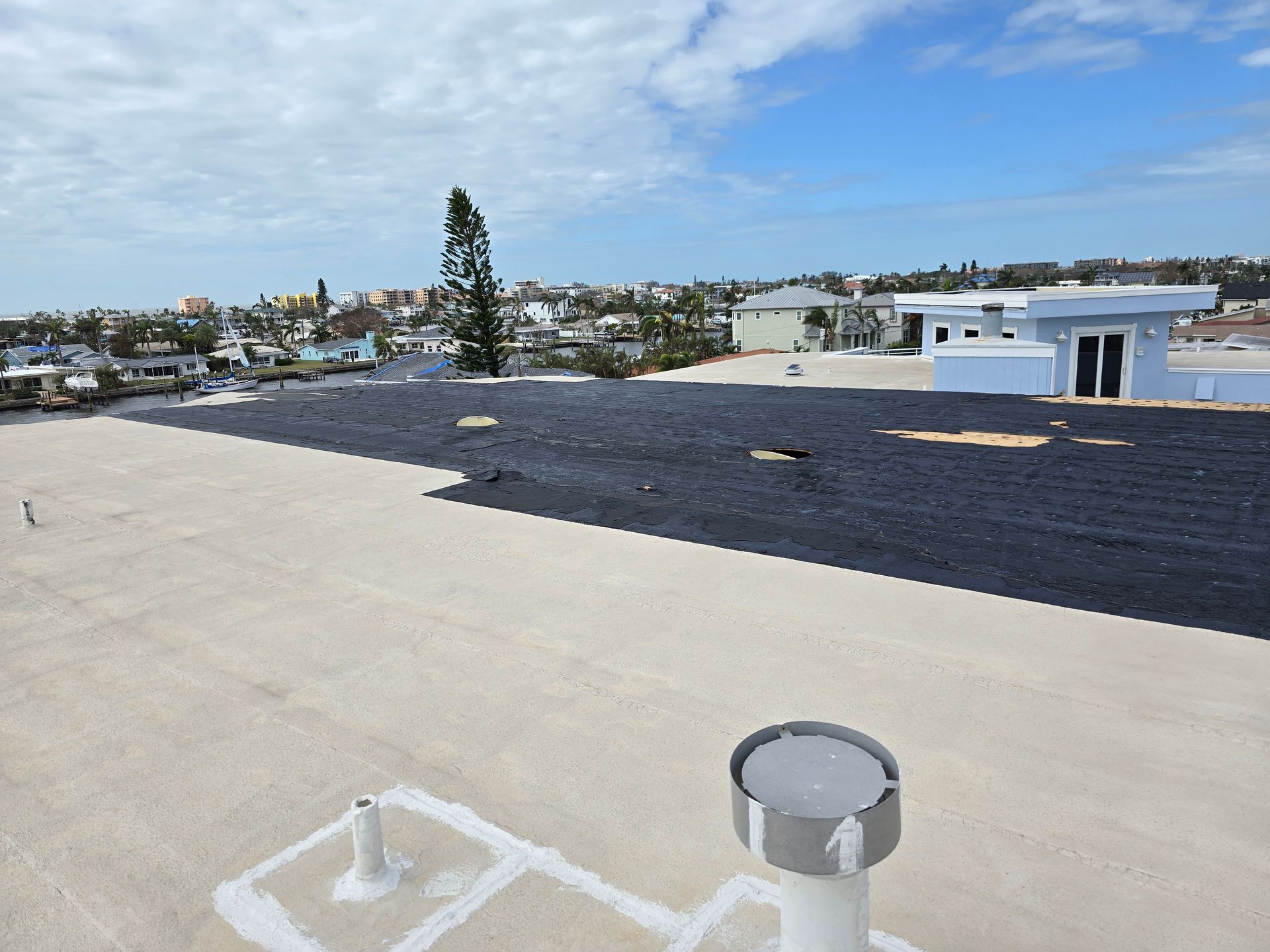 Flat rooftop with dark waterproofing, vents, and a distant city skyline under a blue sky