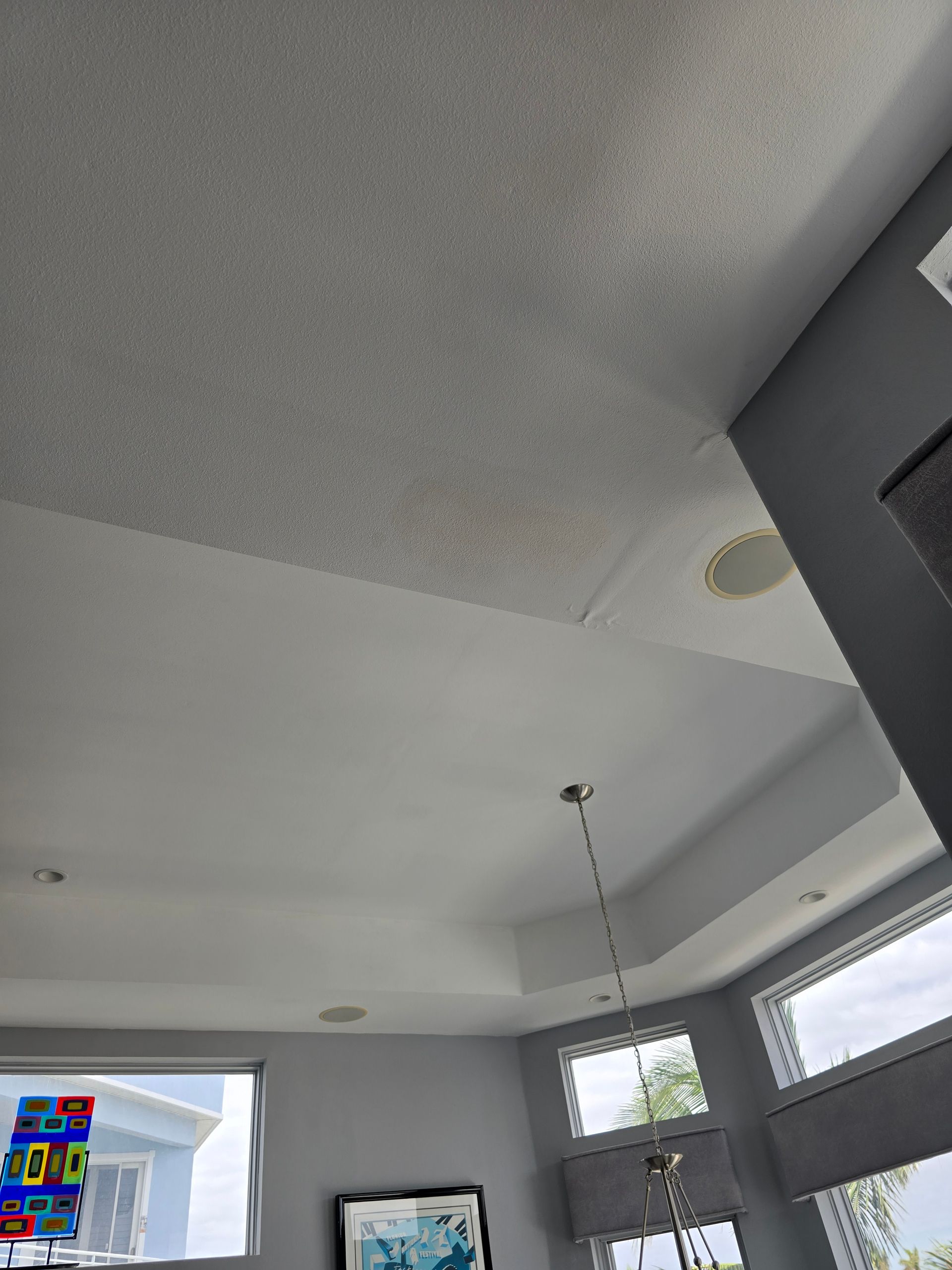 Bright modern living room ceiling with gray walls, recessed lights, windows, and hanging pendant lamp.