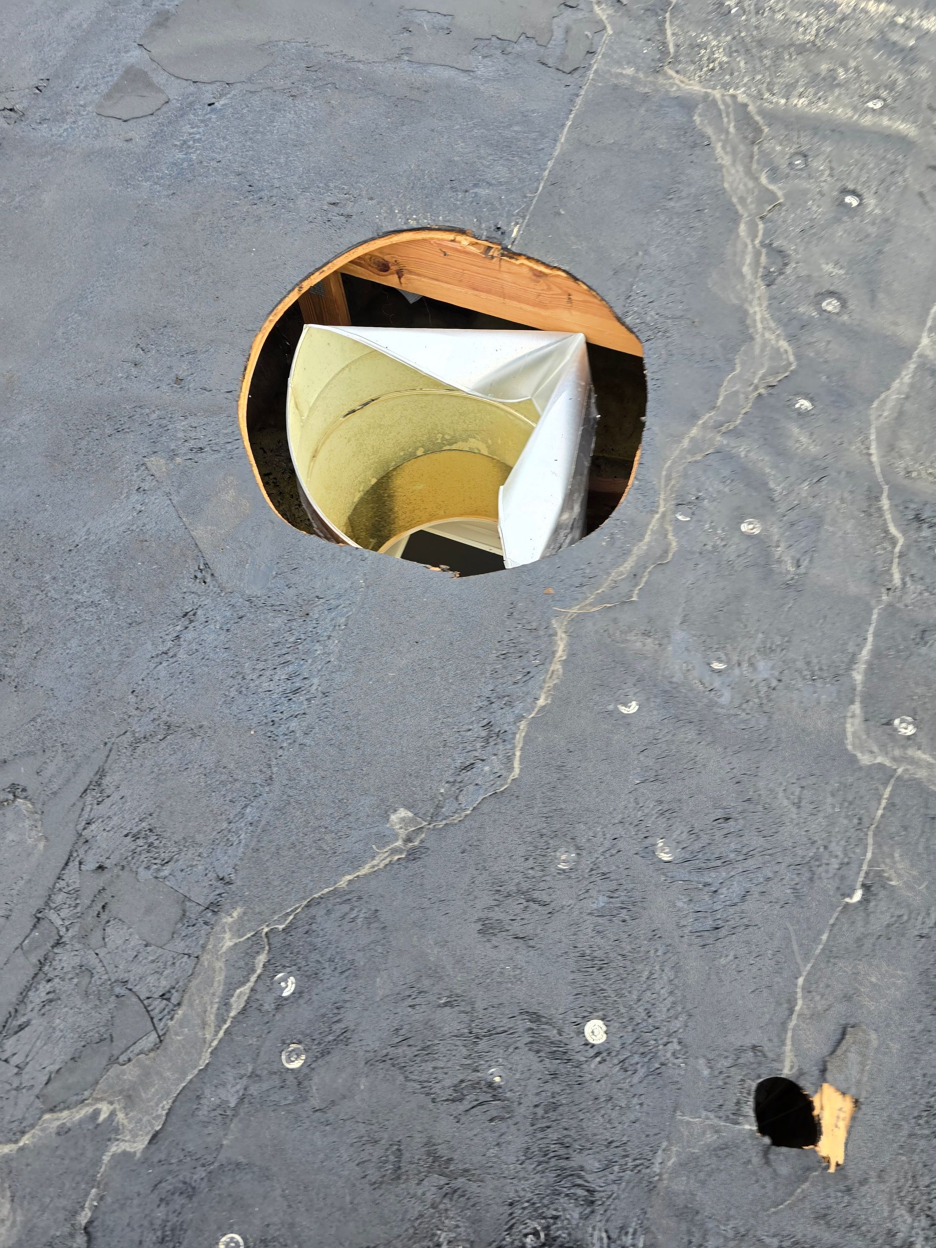 Concrete floor with two circular holes, one large opening revealing a white interior pipe or duct.