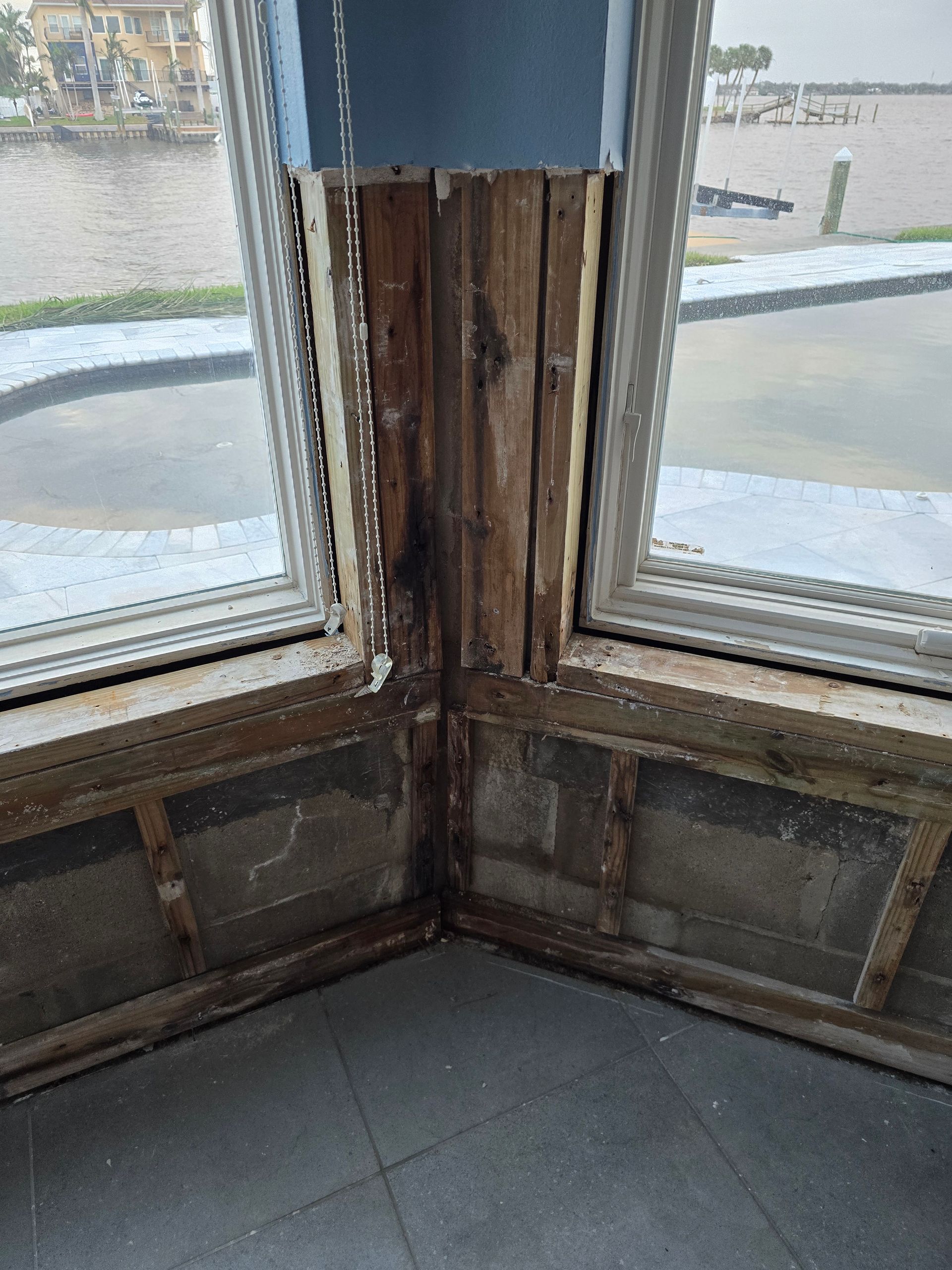 Damaged wooden window corner with exposed rot and peeling paint inside a room