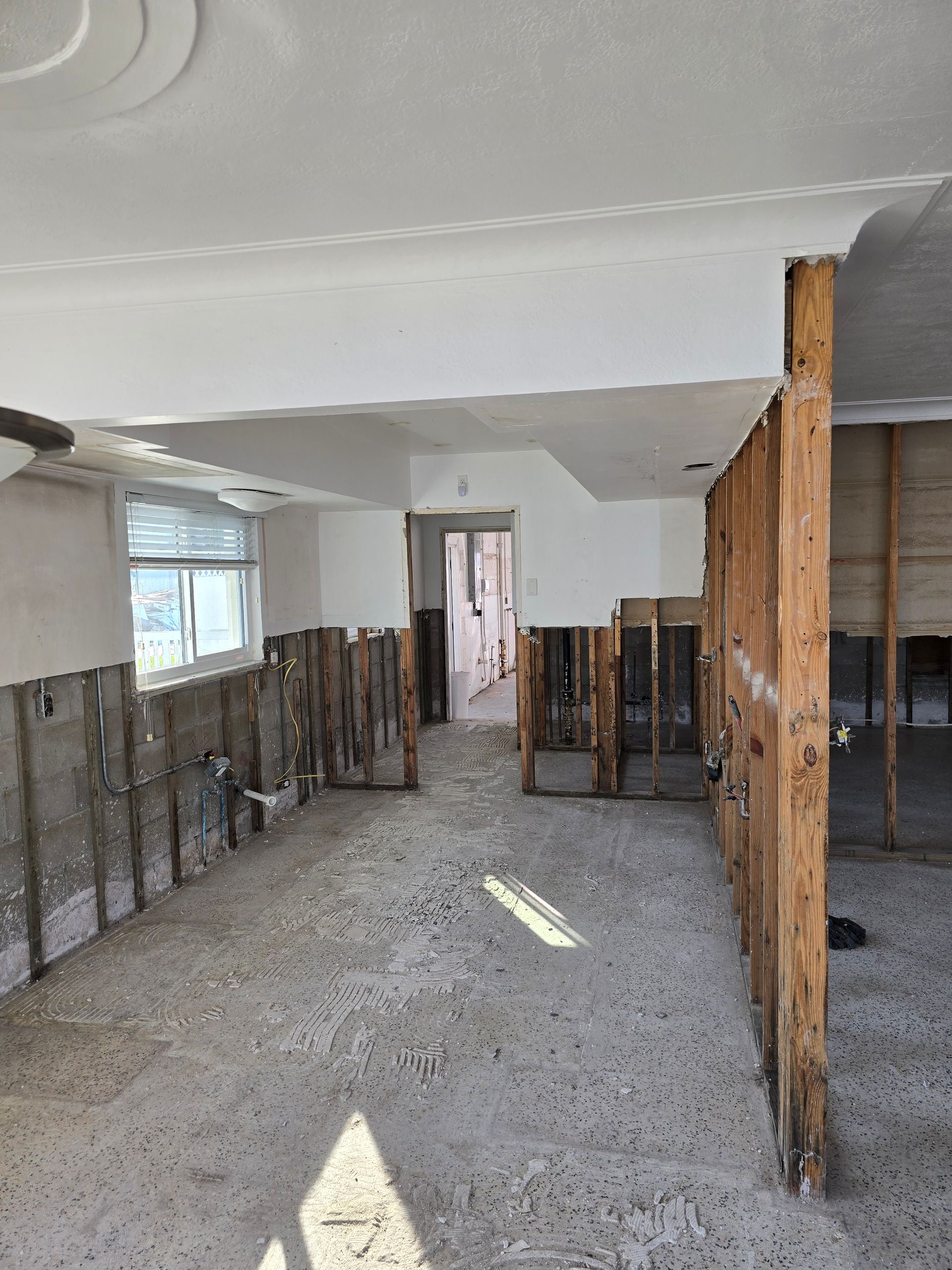 Interior under renovation with exposed wall studs, debris on floor, and a window along the left wall