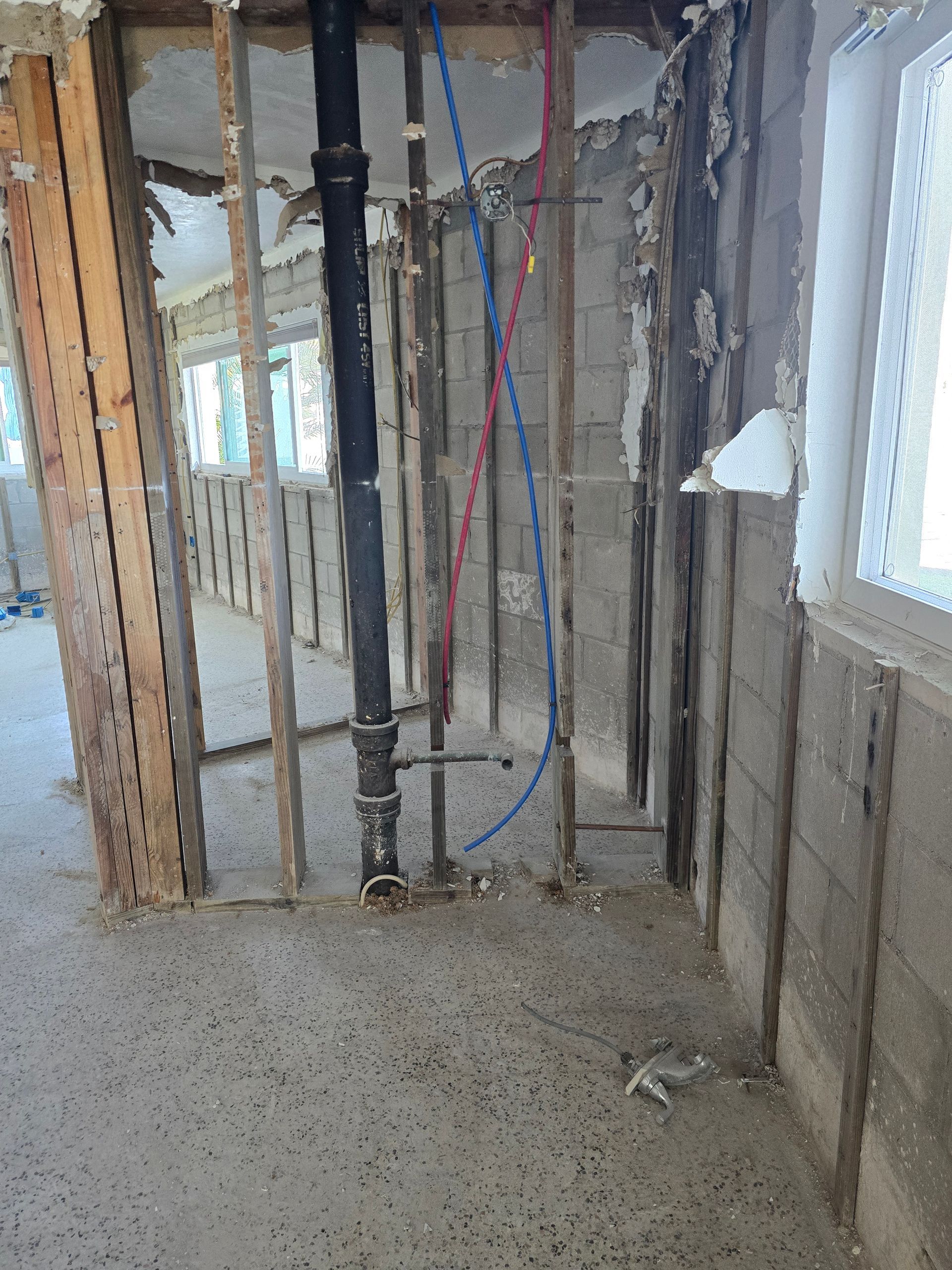 Interior under construction with exposed studs, plumbing pipes, wiring, and unfinished concrete floor.
