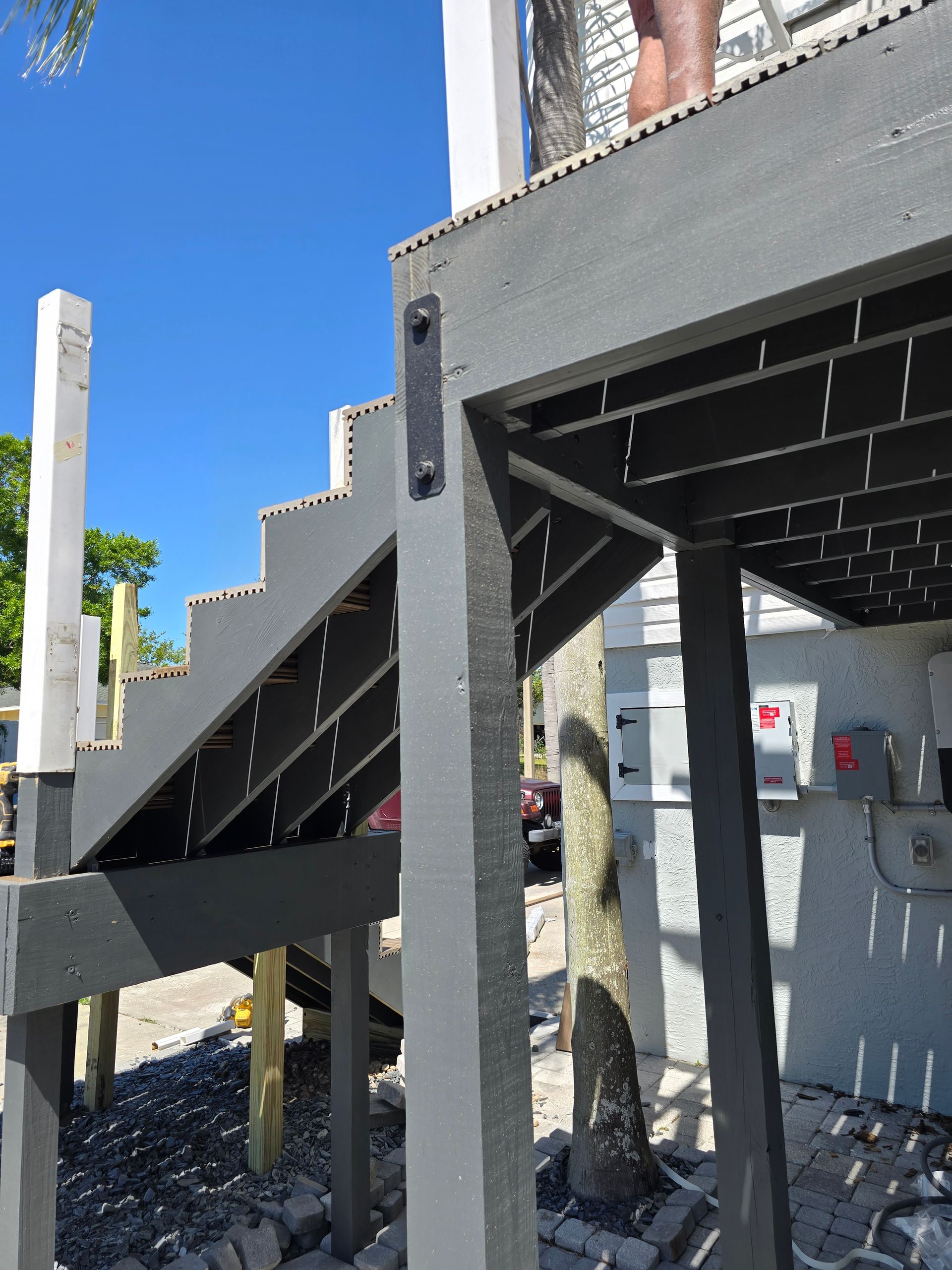 Outdoor staircase beside a gray building, with black steps and white posts under a clear blue sky