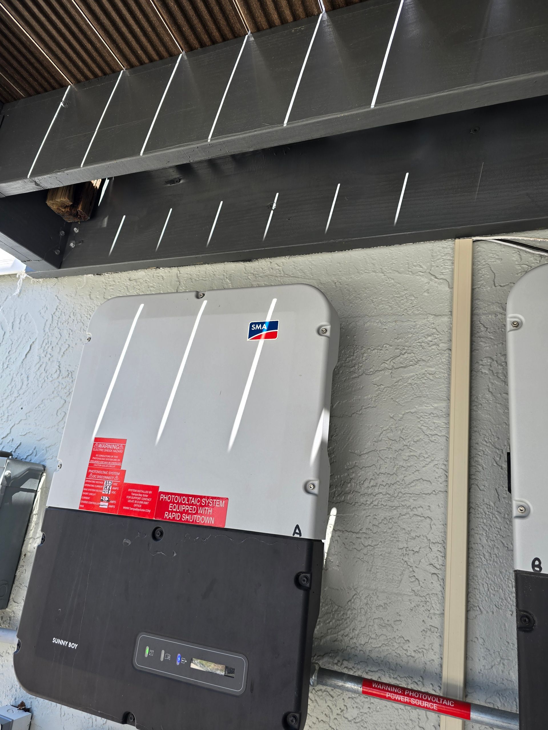 Close-up of two wall-mounted electrical boxes with conduit beneath a black overhang