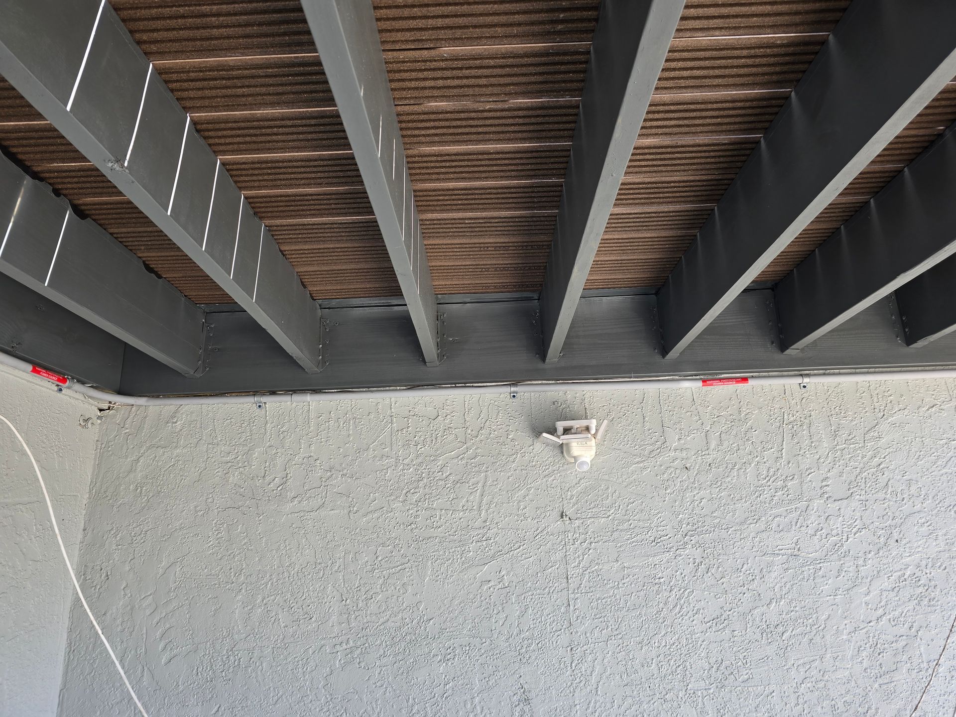 Underside of a bridge with dark steel beams and wooden planks above a gray concrete wall below