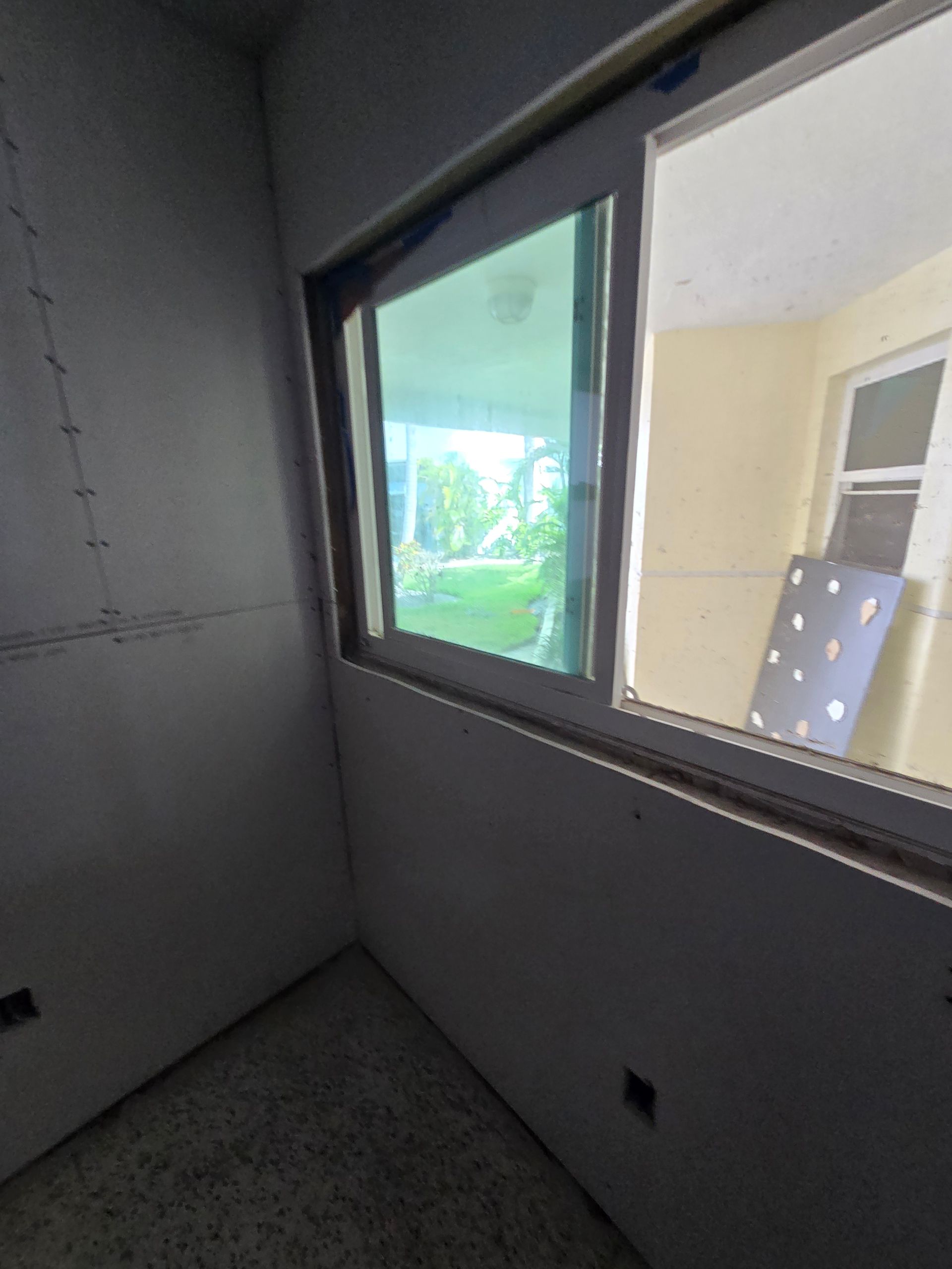 Empty unfinished room with gray walls, carpet, and a large window overlooking a balcony and greenery