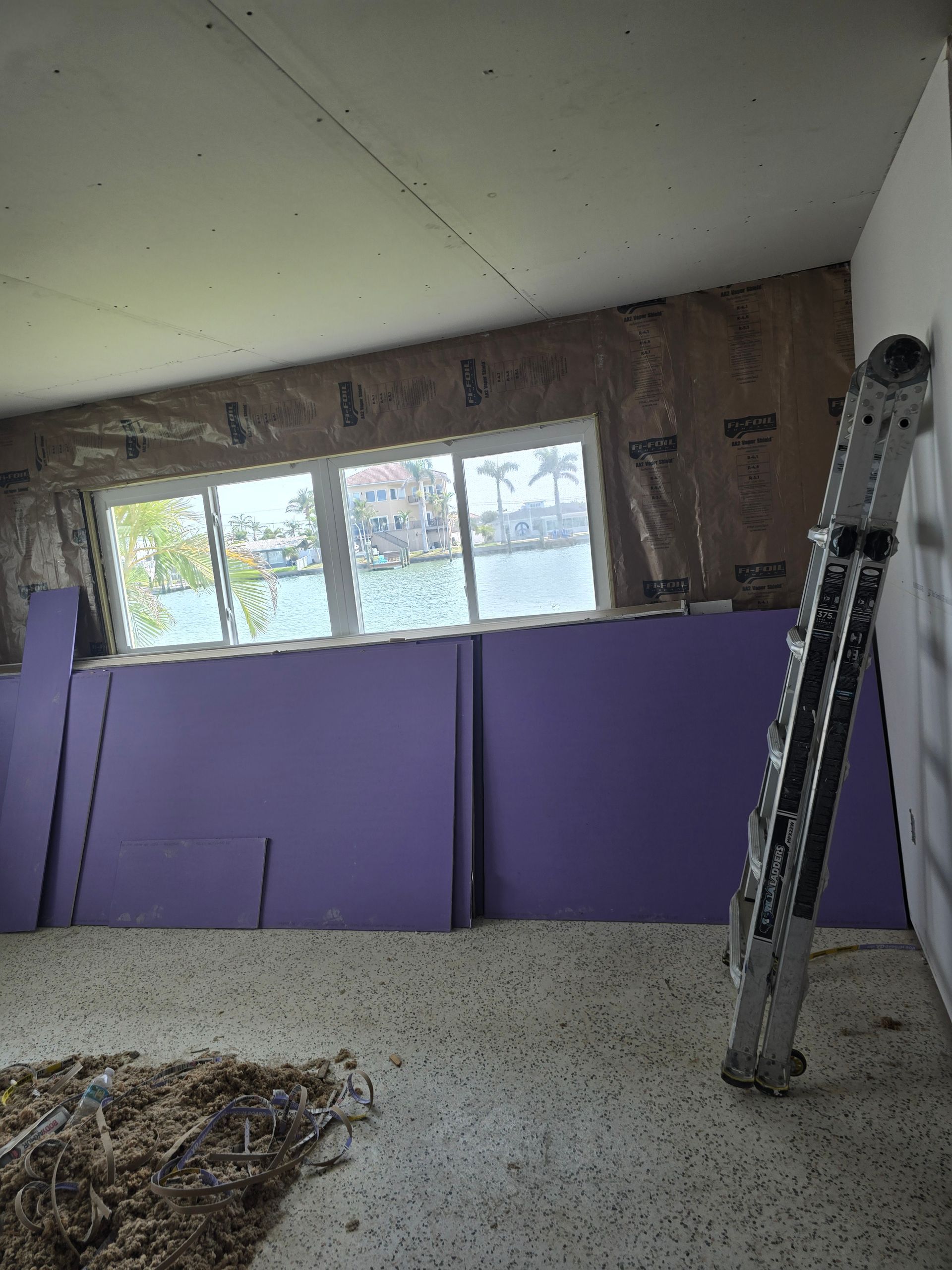 Renovation room with purple wall panels, ladder, and window light on bare floor