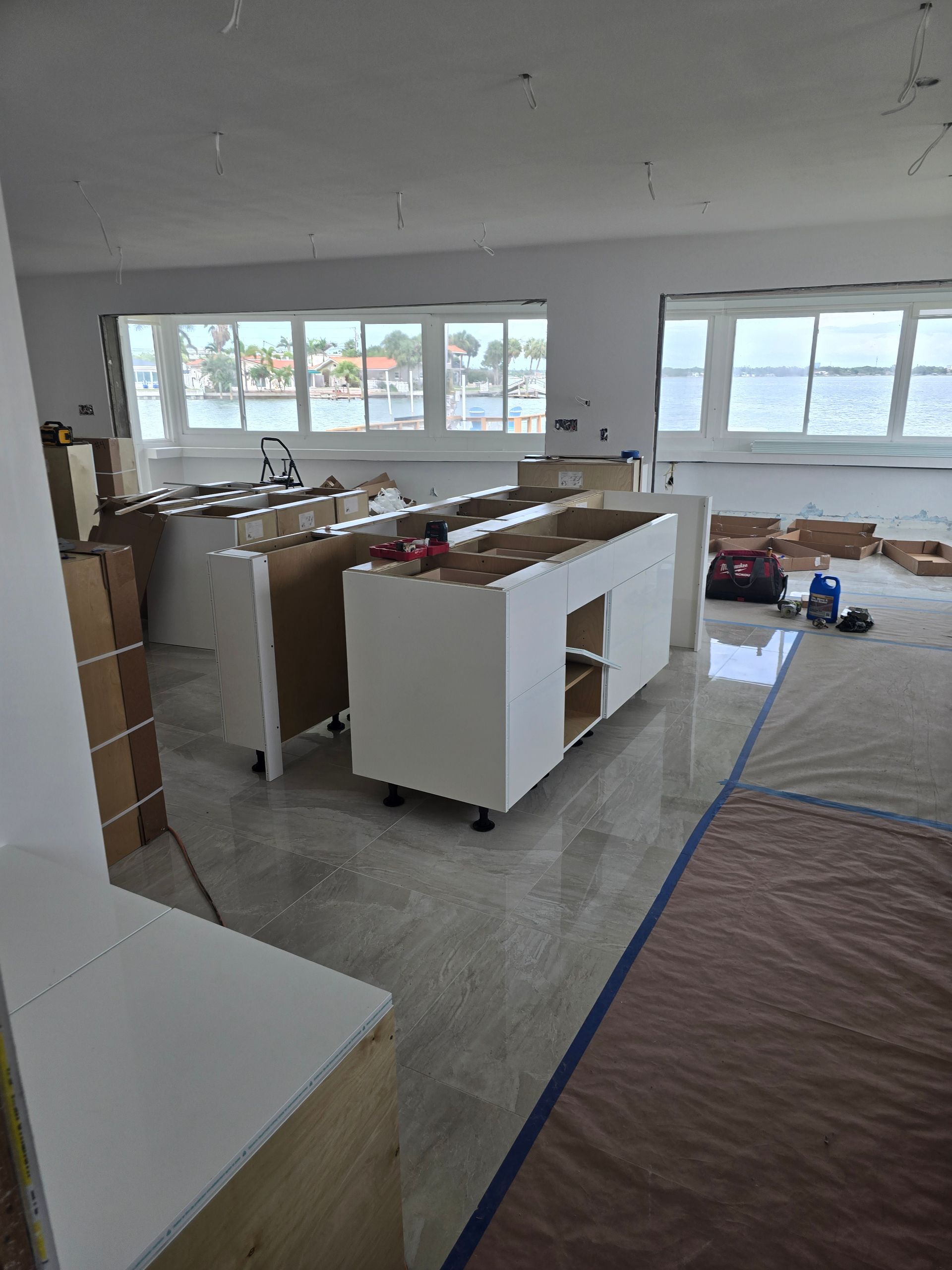 Unfinished kitchen with white cabinets, concrete floor, and large windows in a bare room.