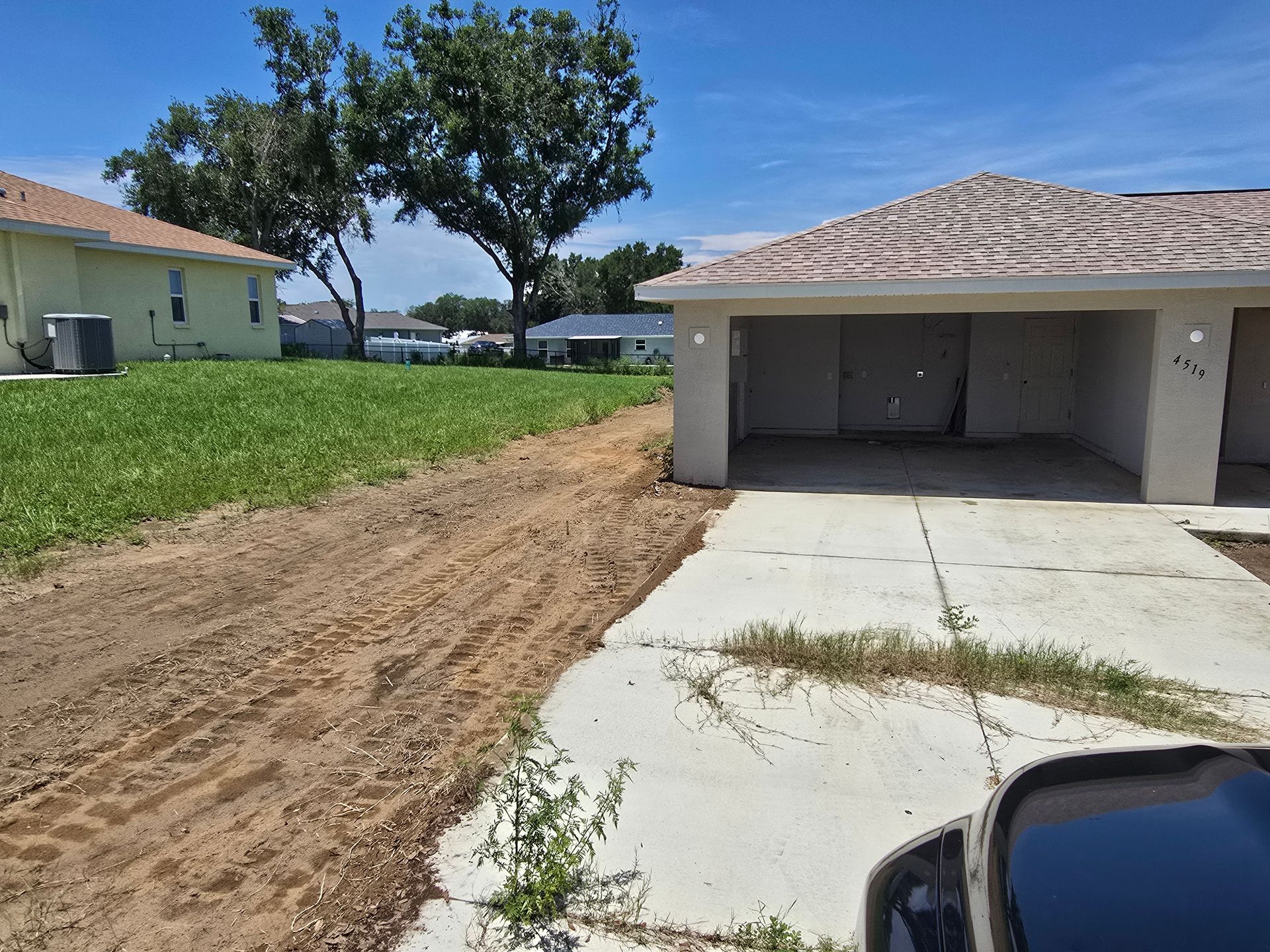Driveway beside a two-car garage with dirt landscaping and a large tree in the yard