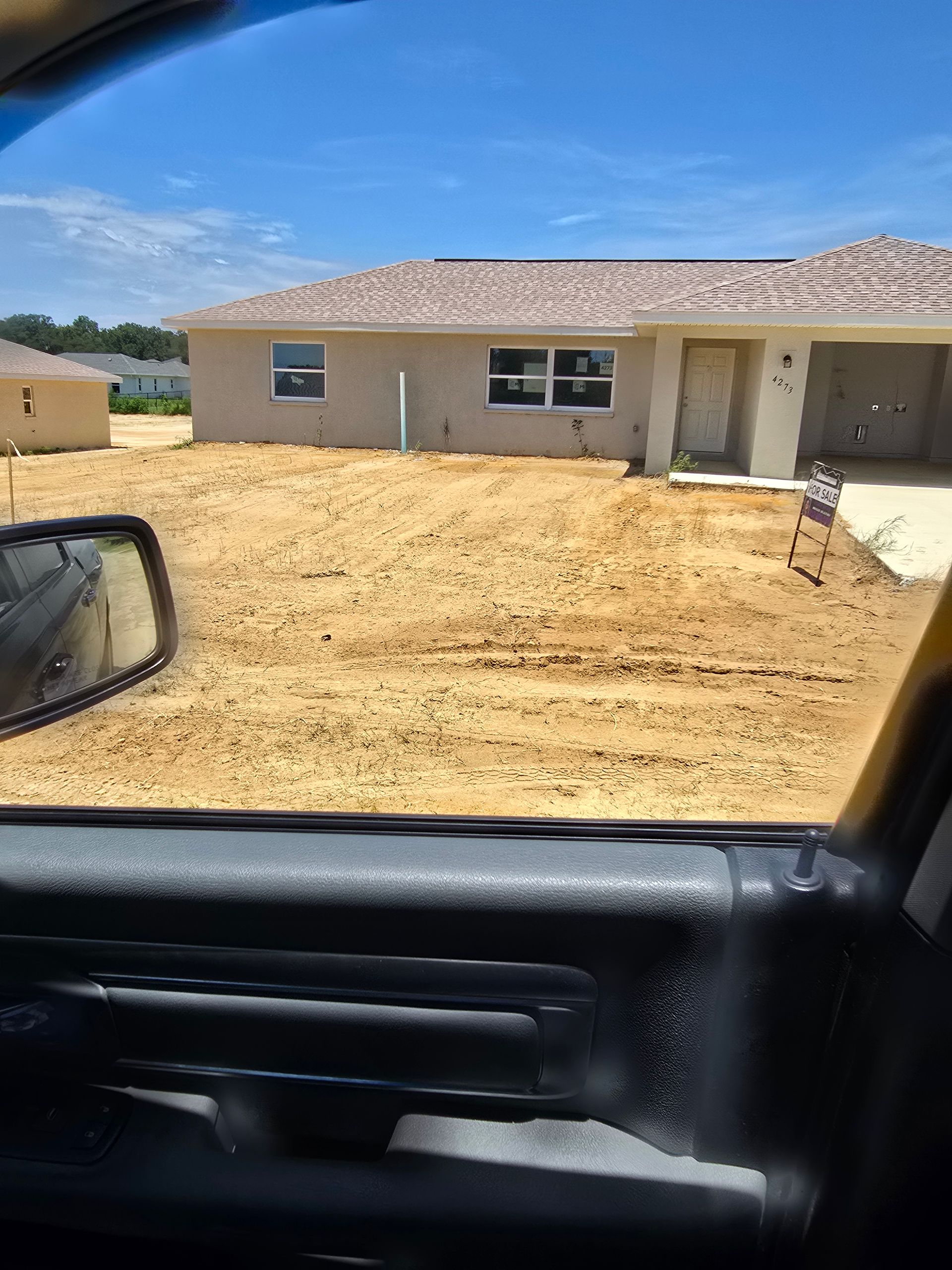 Single-story house under construction with bare dirt yard, seen from inside a car.