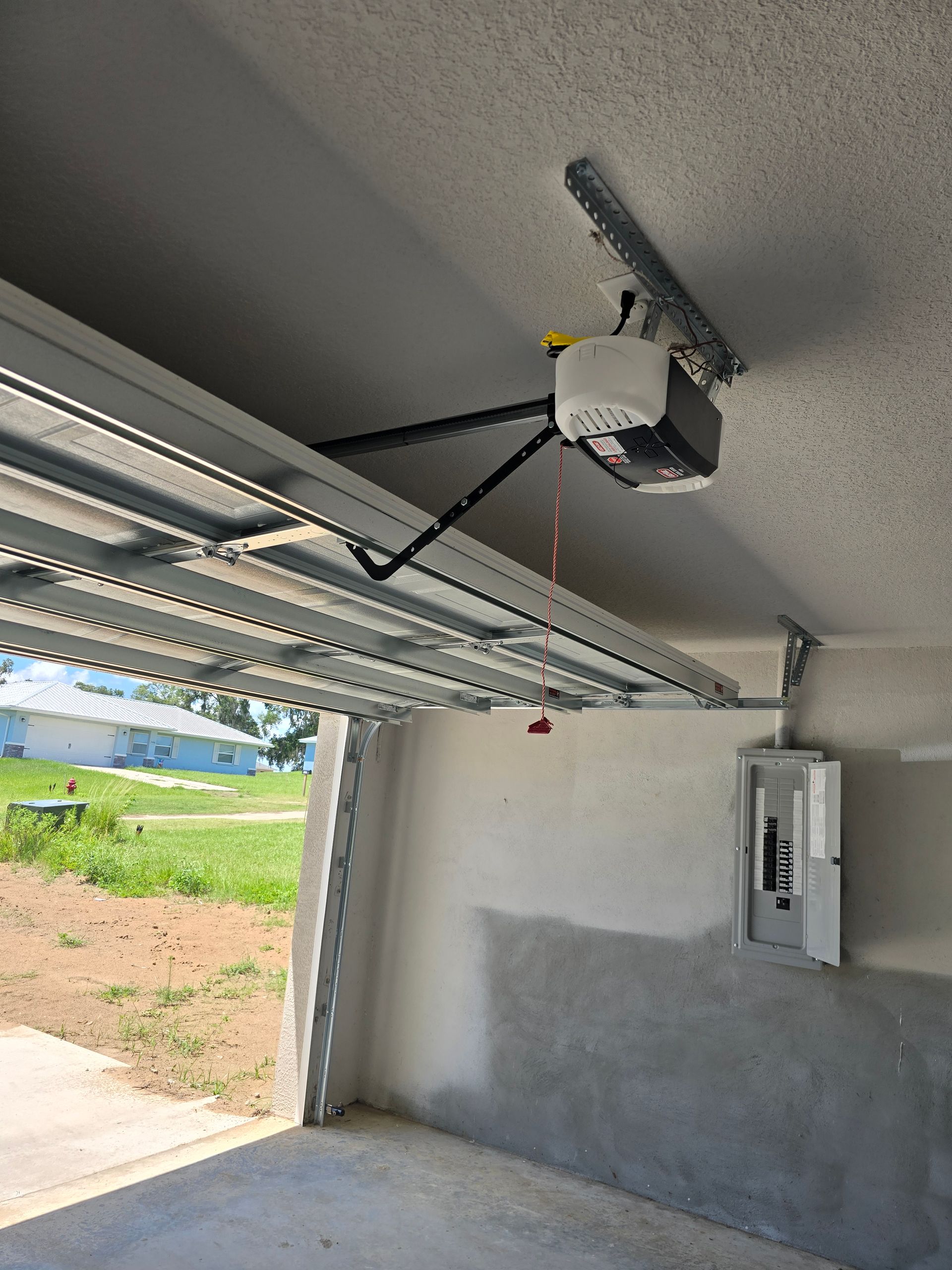 Garage interior with open overhead door, ceiling opener, and side wall control panel.