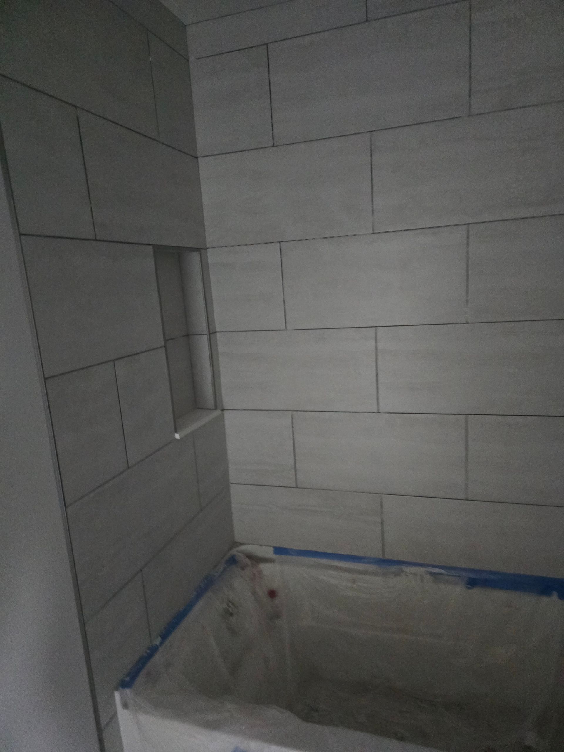 Tiled bathroom shower under construction with unfinished walls and a tub edge wrapped in blue tape