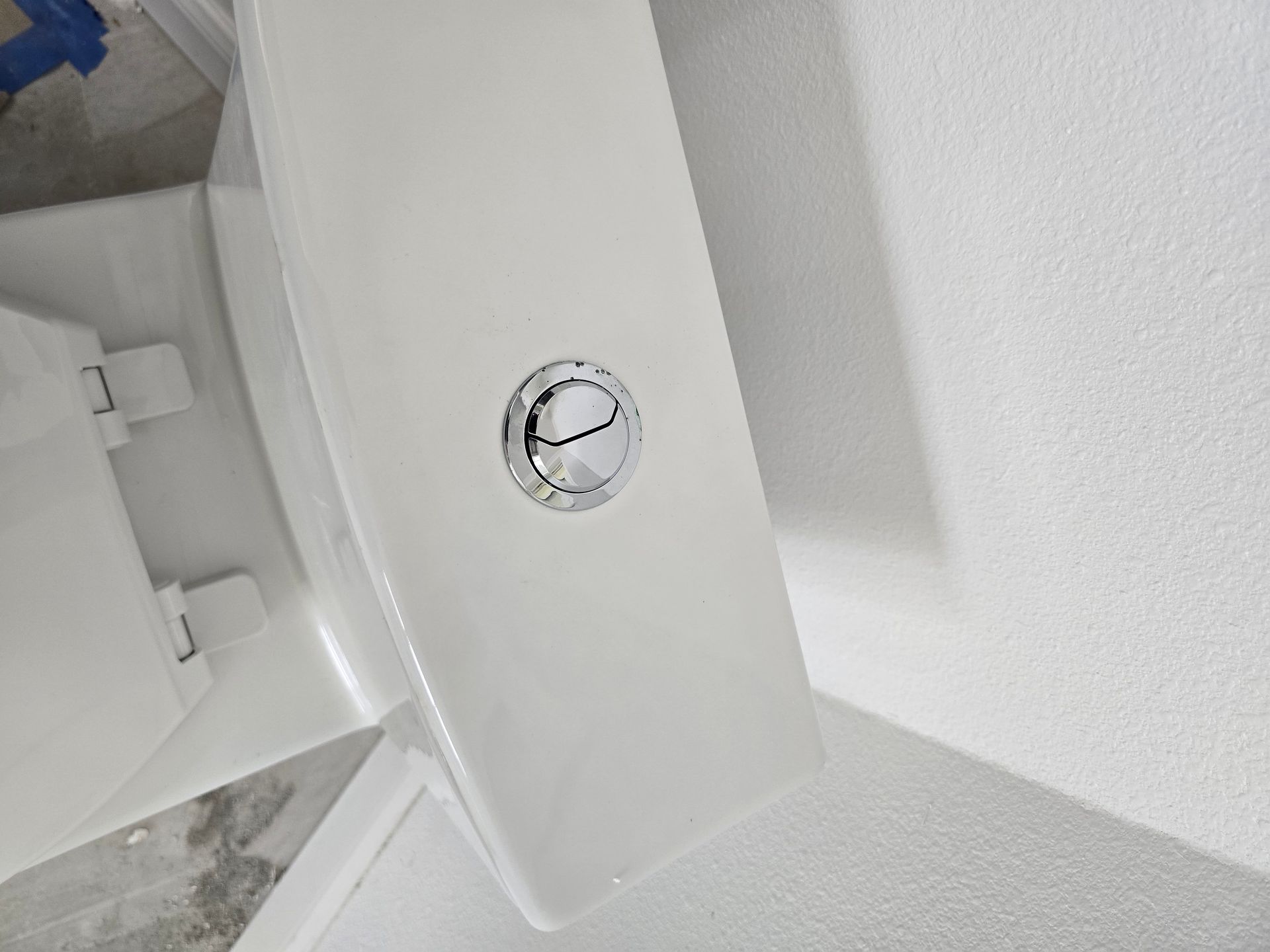 Close-up of a white toilet tank with a chrome flush button on a bathroom wall.