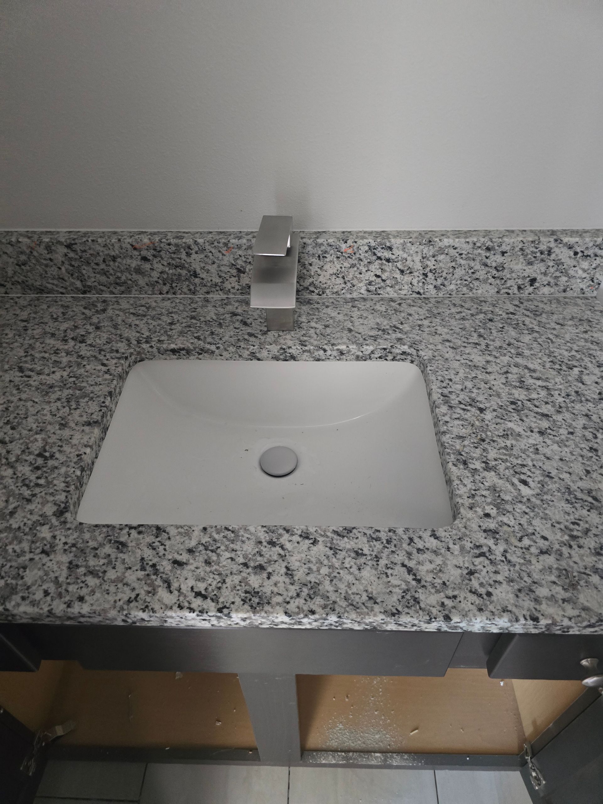 White bathroom sink in speckled granite countertop with a chrome faucet and wall mirror above