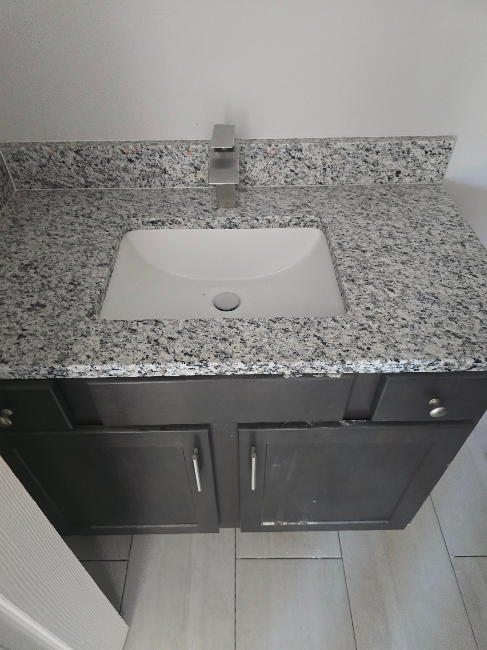 Bathroom vanity with speckled granite countertop, white sink, and dark wood cabinet below.