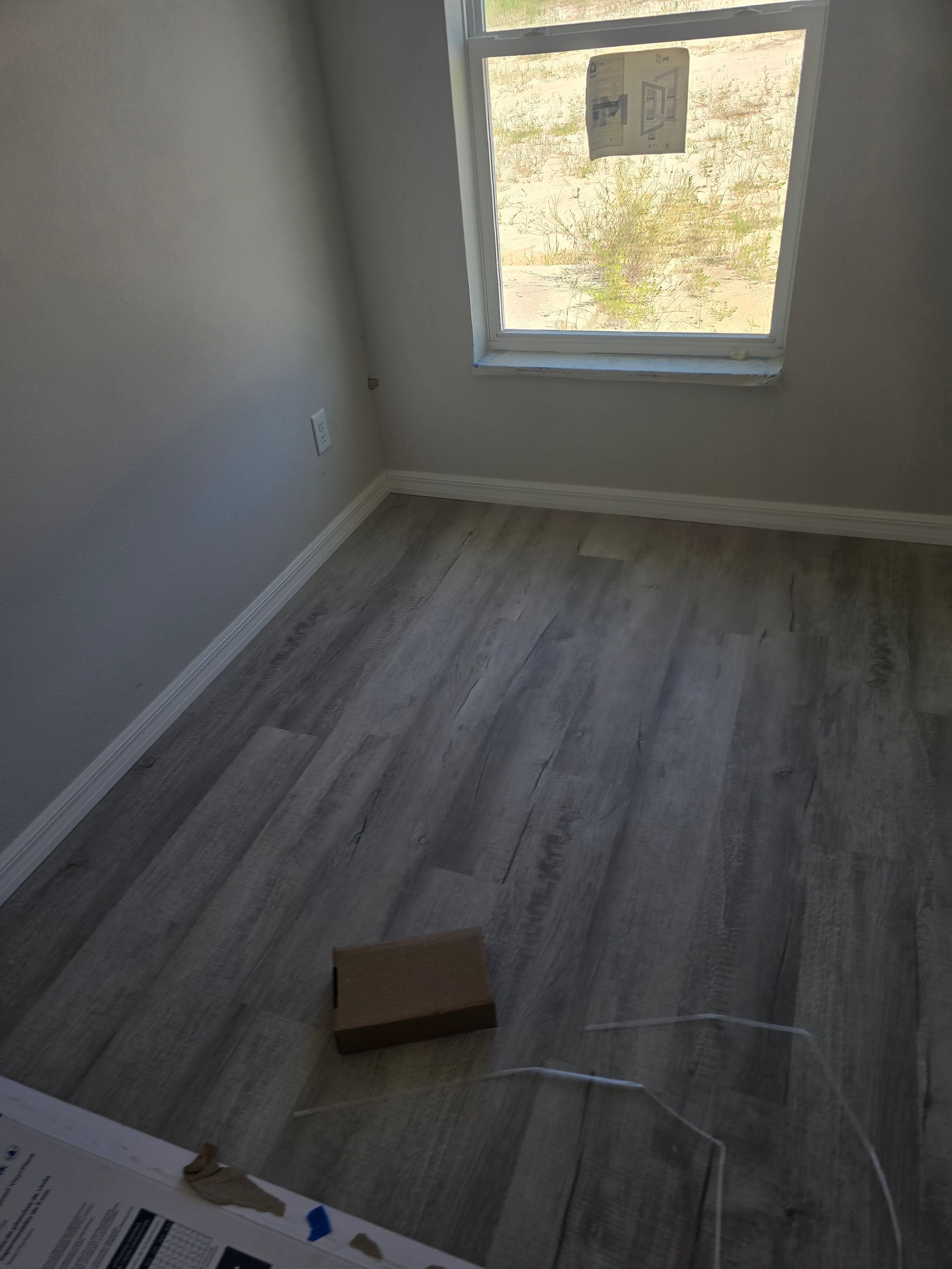 Empty room with gray wood flooring, white walls, and a window letting in daylight.