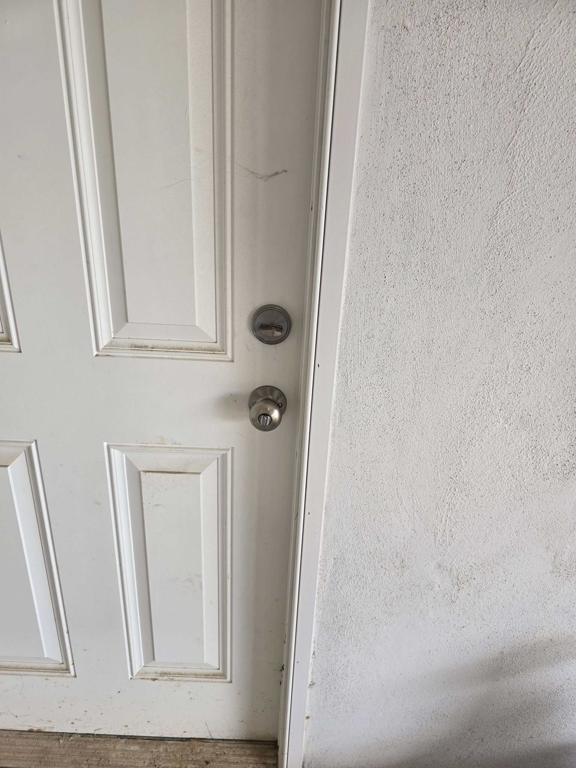 Close-up of a white paneled door with a silver doorknob beside a textured gray wall.