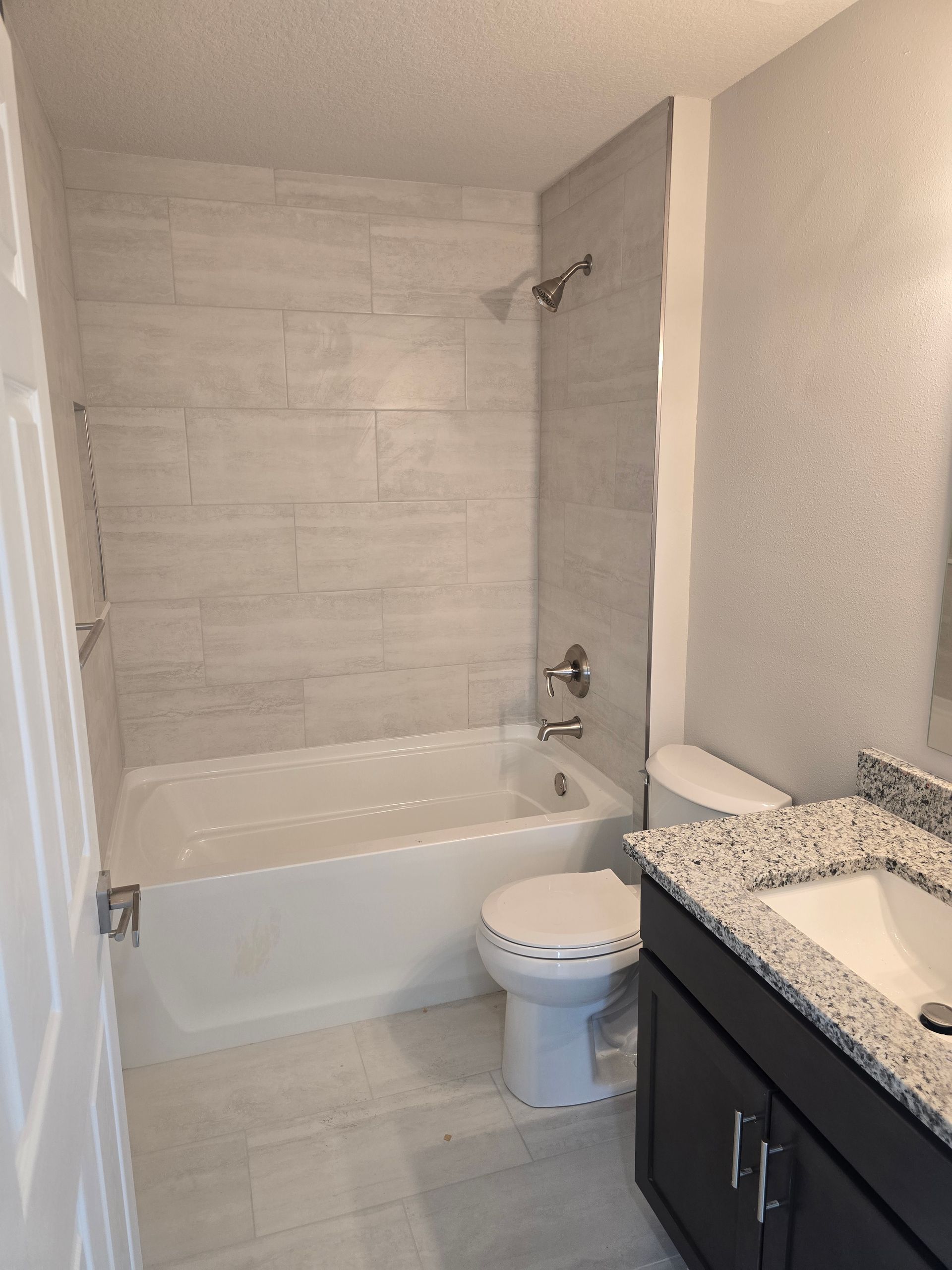 Small bathroom with tub-shower, toilet, and dark vanity with speckled countertop.