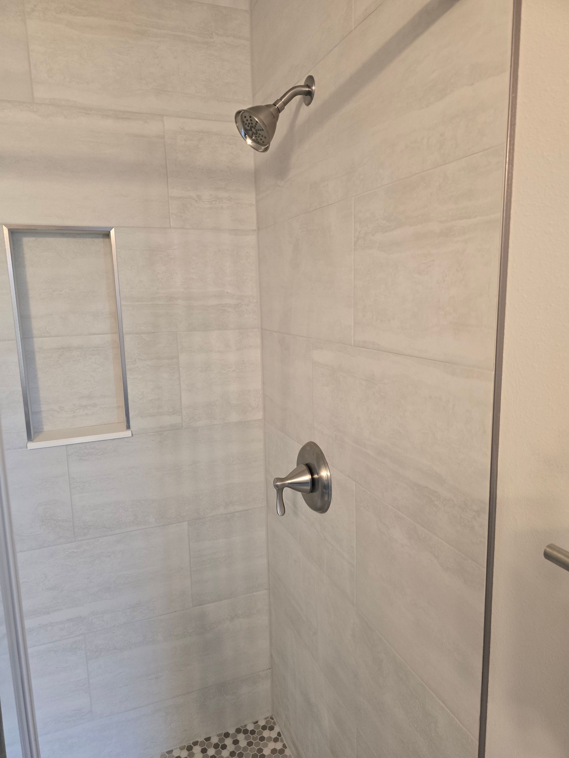 Shower stall with tiled walls, rainfall showerhead, and built-in niche shelf