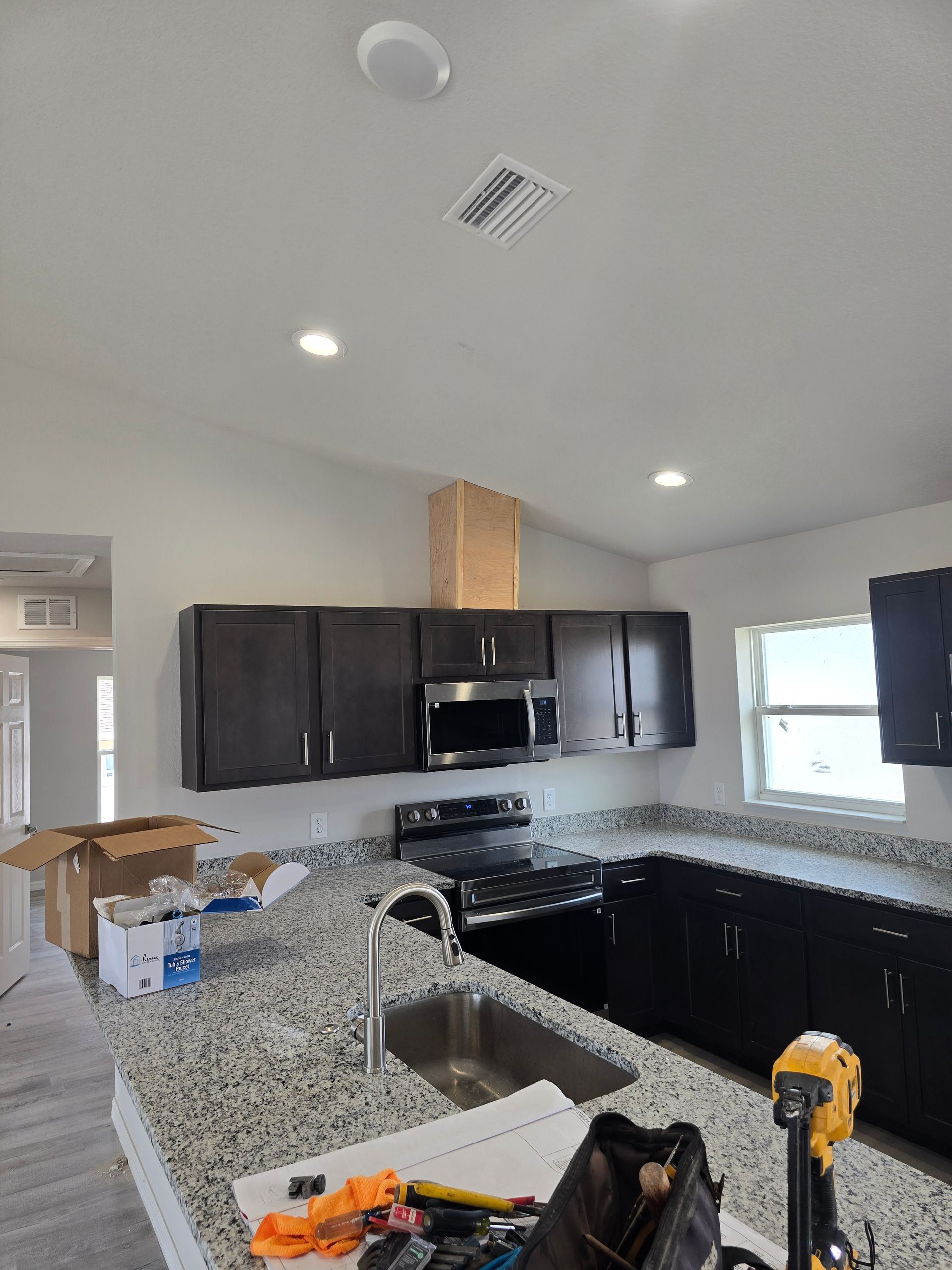 Partially renovated kitchen with dark cabinets, granite counters, stainless stove, and boxes on the counter