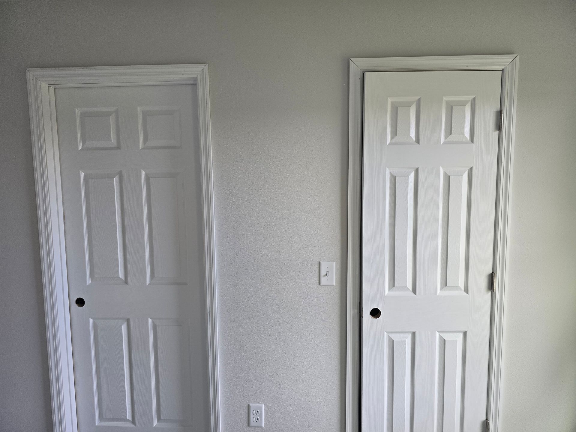 Two white interior doors on a light gray wall, with visible trim and a light switch between them