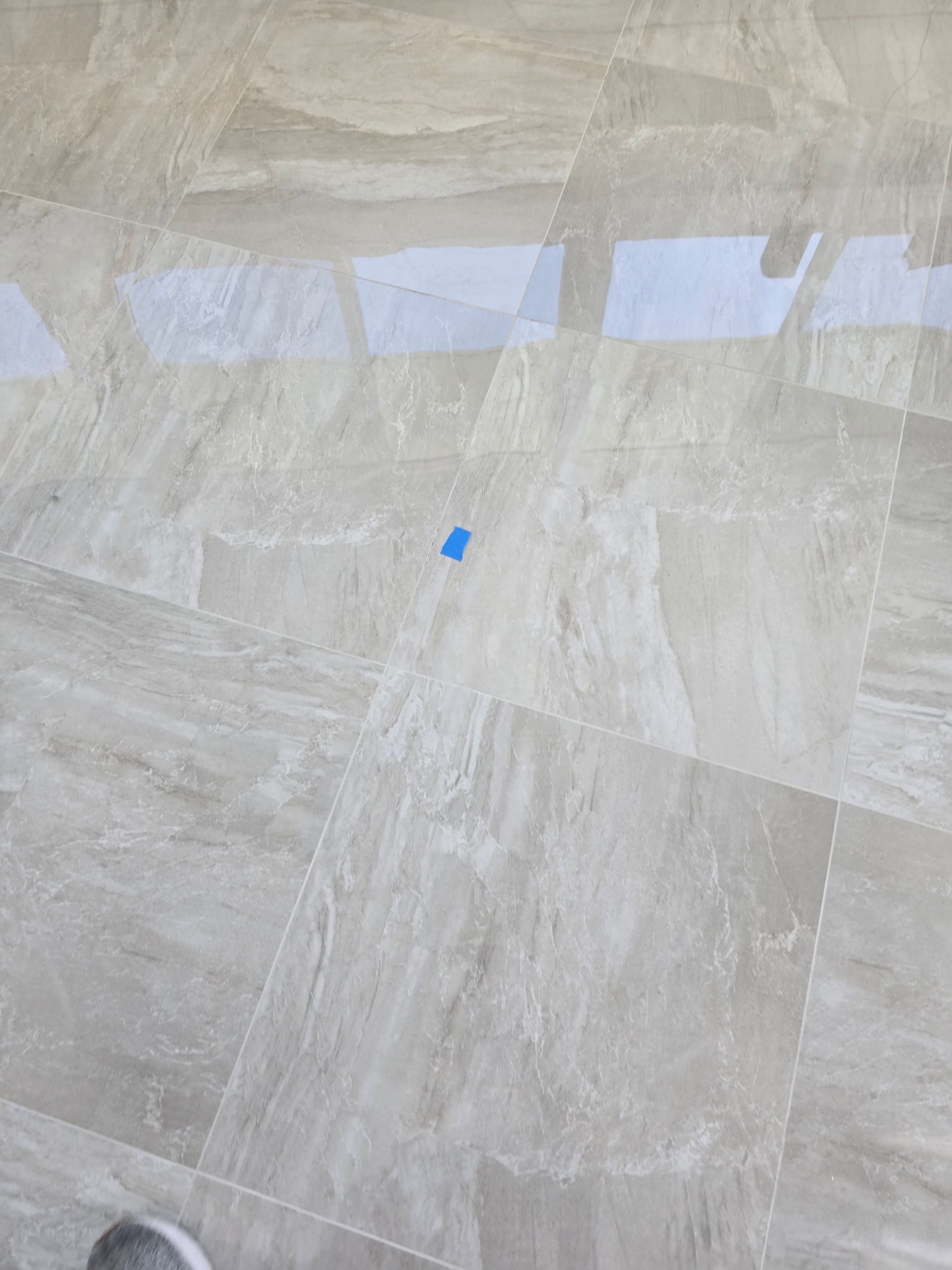 Light gray stone floor with window reflections and a small blue tape mark near the center