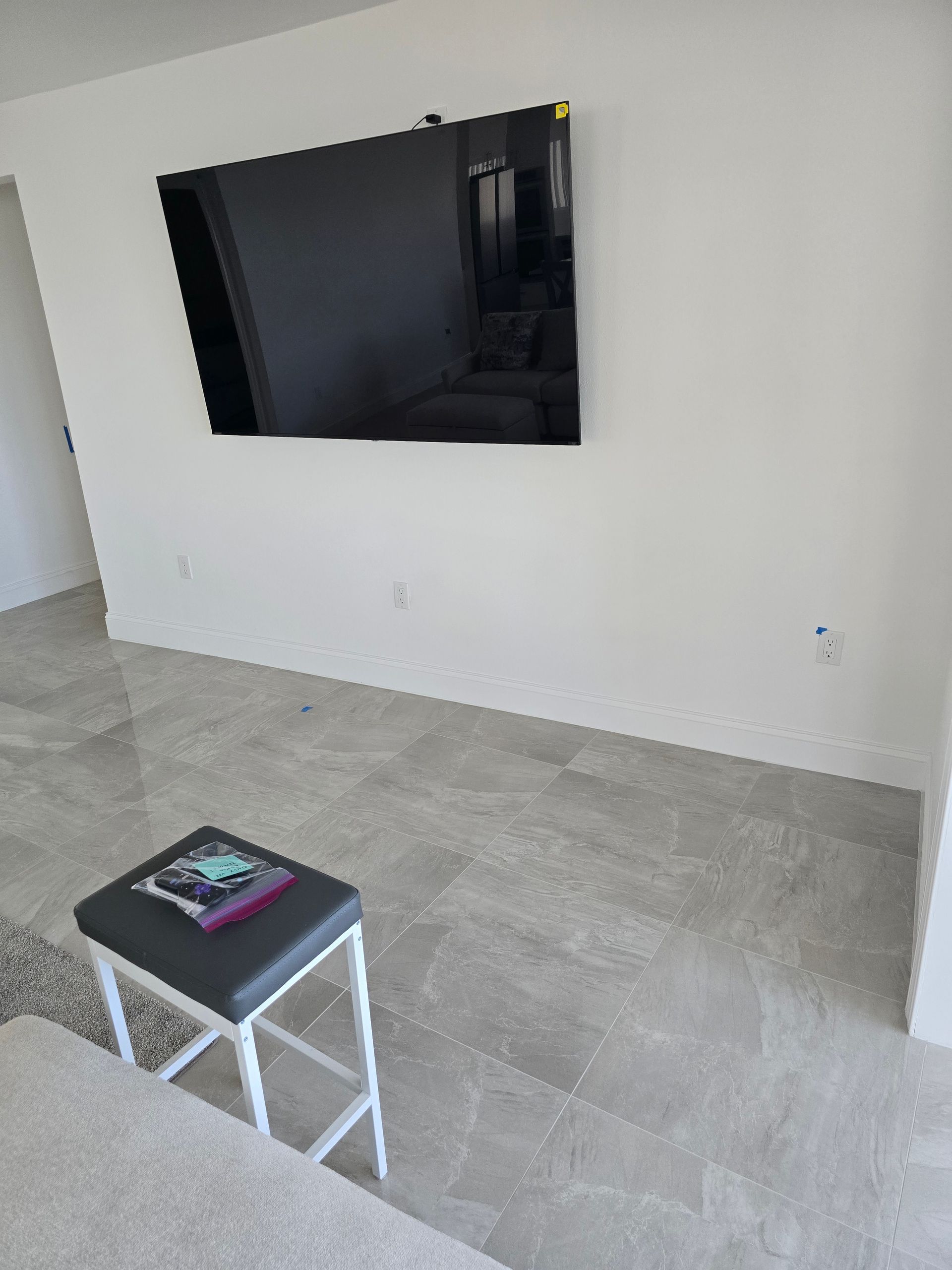 Living room with wall-mounted TV, gray tile floor, and a small stool holding a magazine
