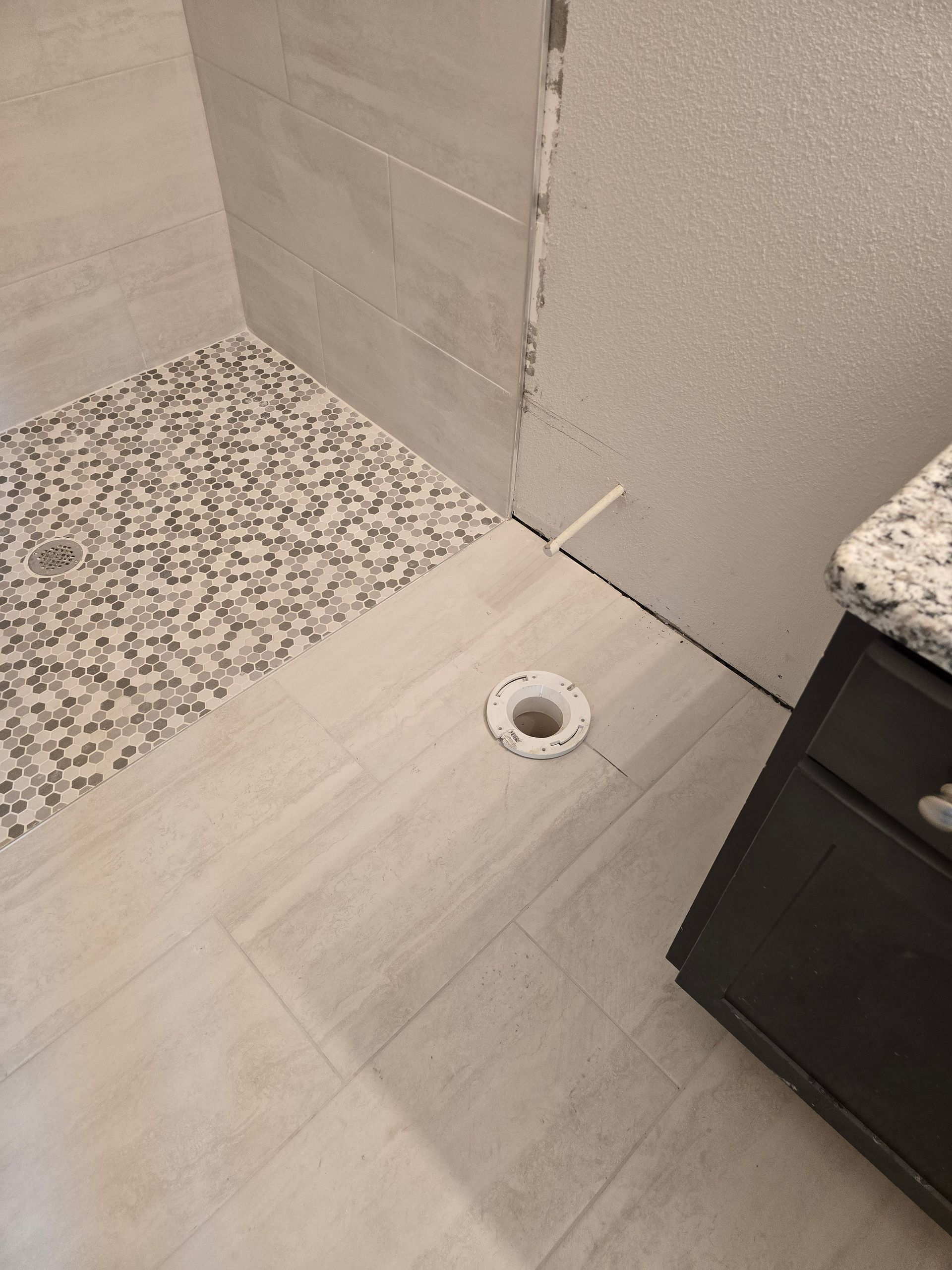 Bathroom floor corner with a circular drain and a dark cabinet edge.