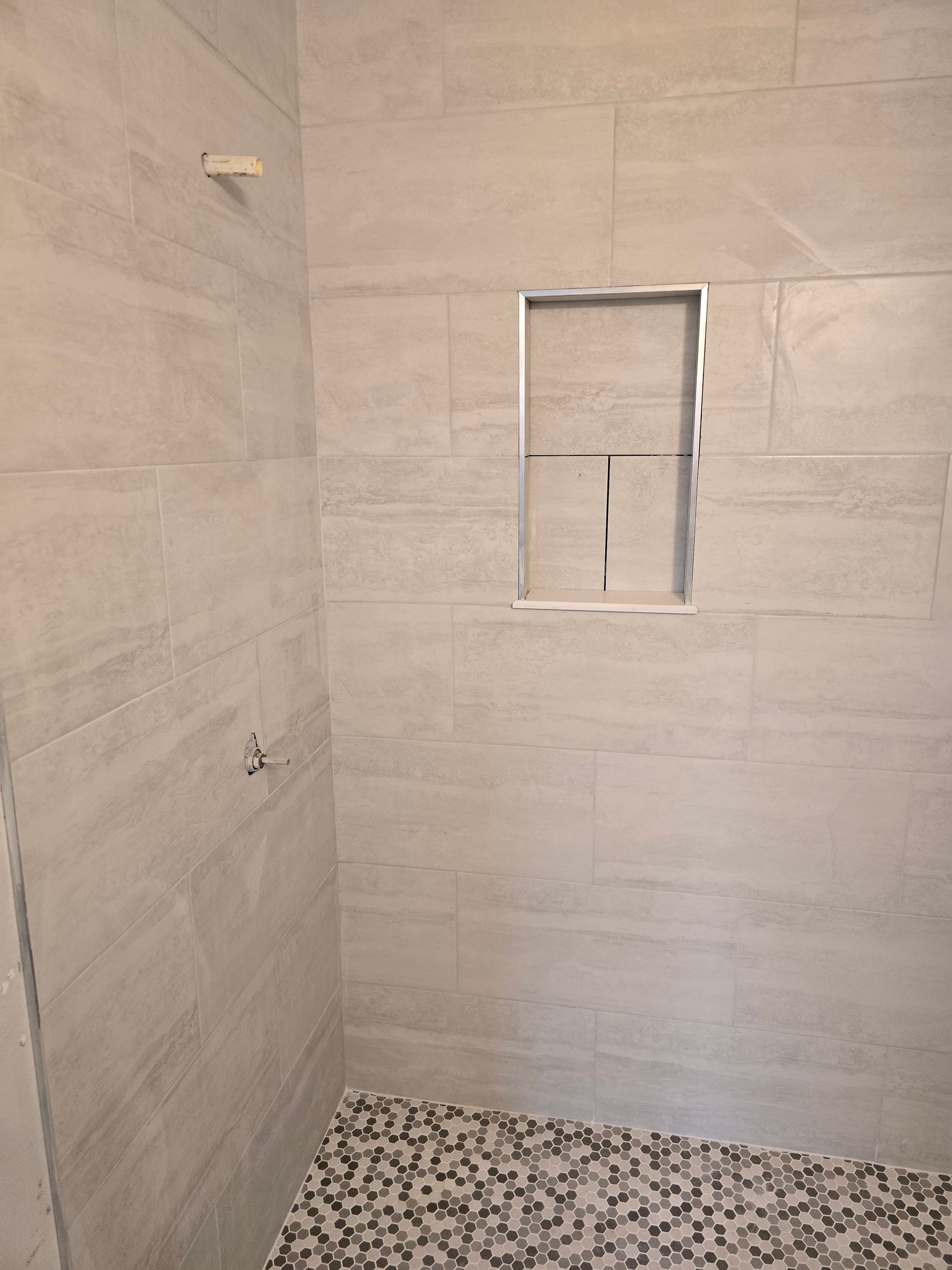 Empty tiled shower with a small recessed window and pebble floor.