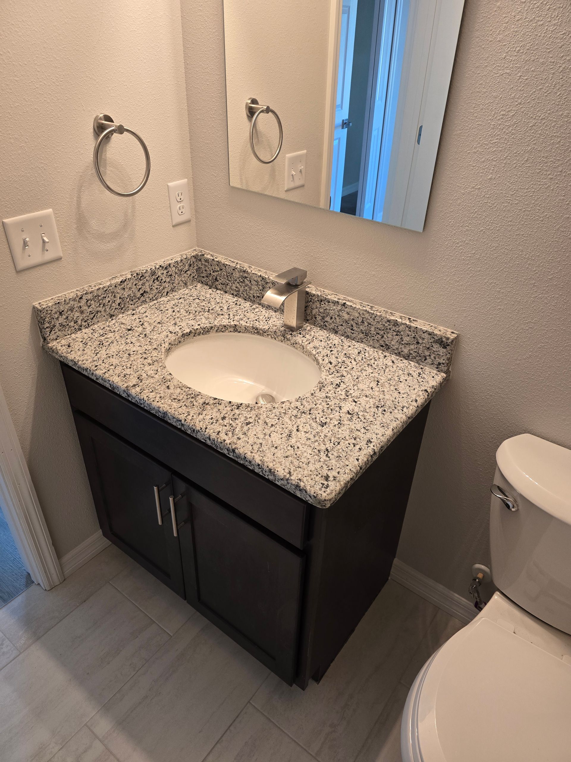 Small bathroom vanity with speckled countertop, mirror, towel ring, and toilet beside it