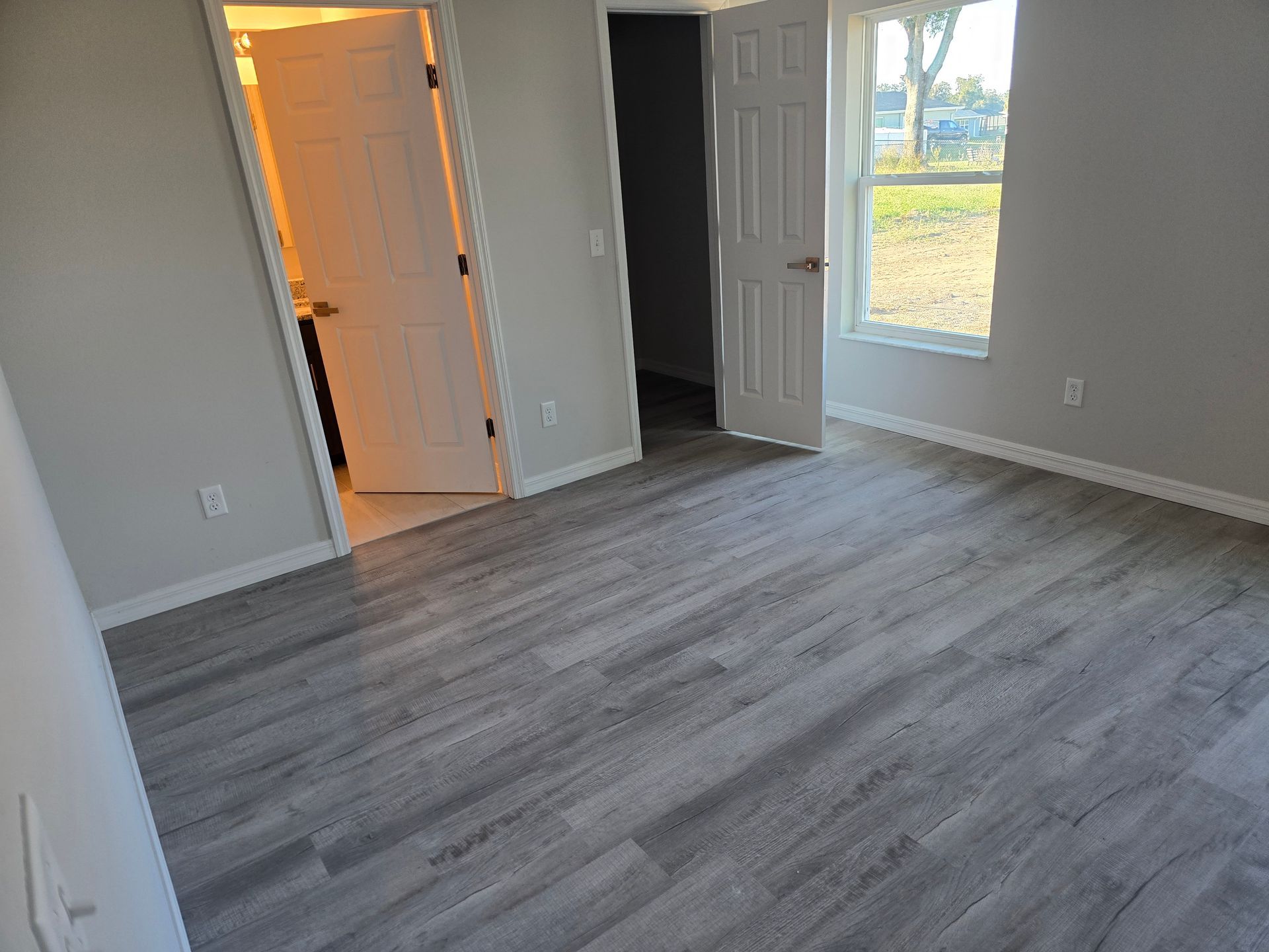 Empty gray bedroom with wood-look flooring, open closet door, and window overlooking trees