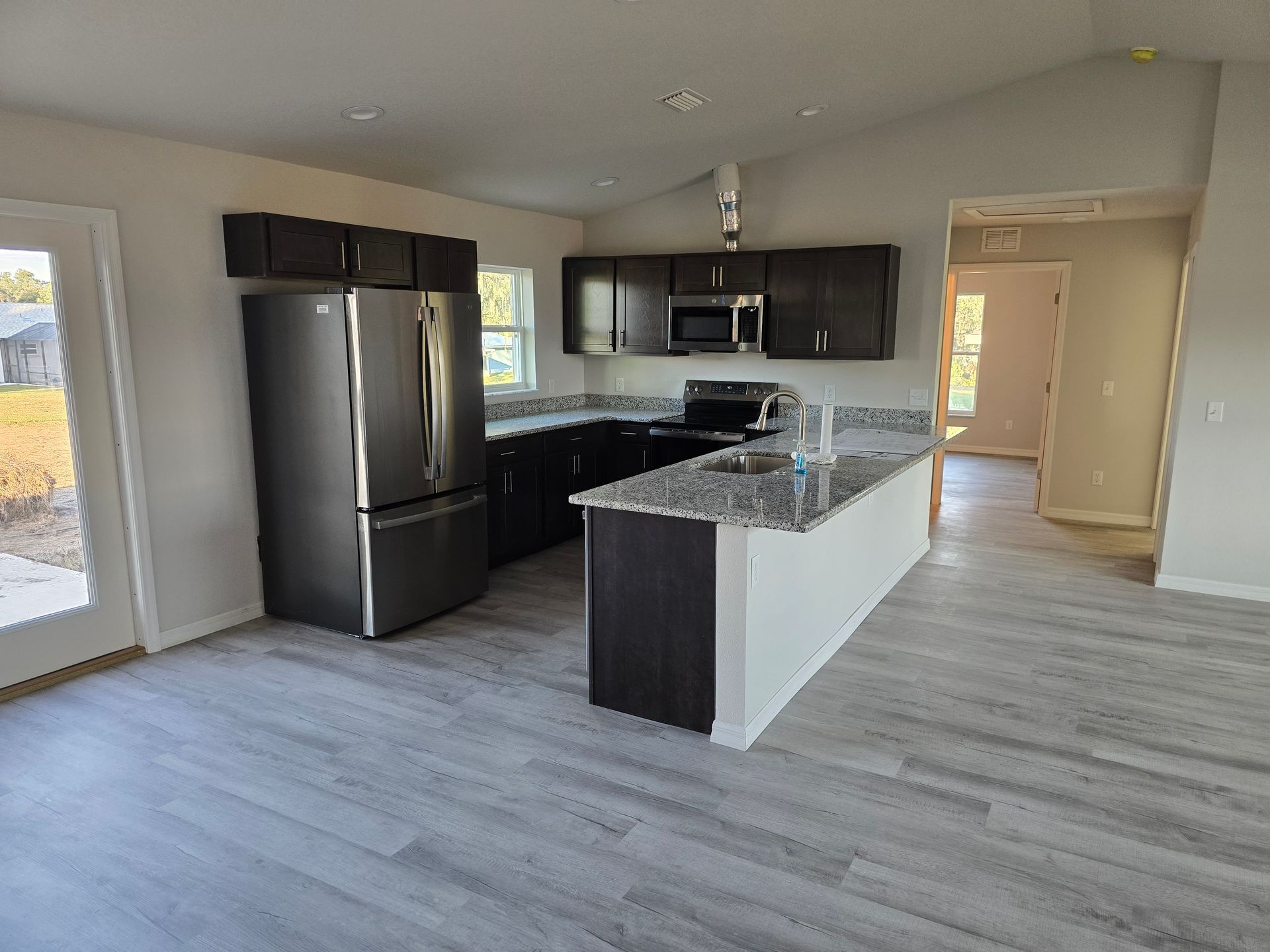 Modern kitchen with dark cabinets, stainless appliances, granite island, and light wood floors