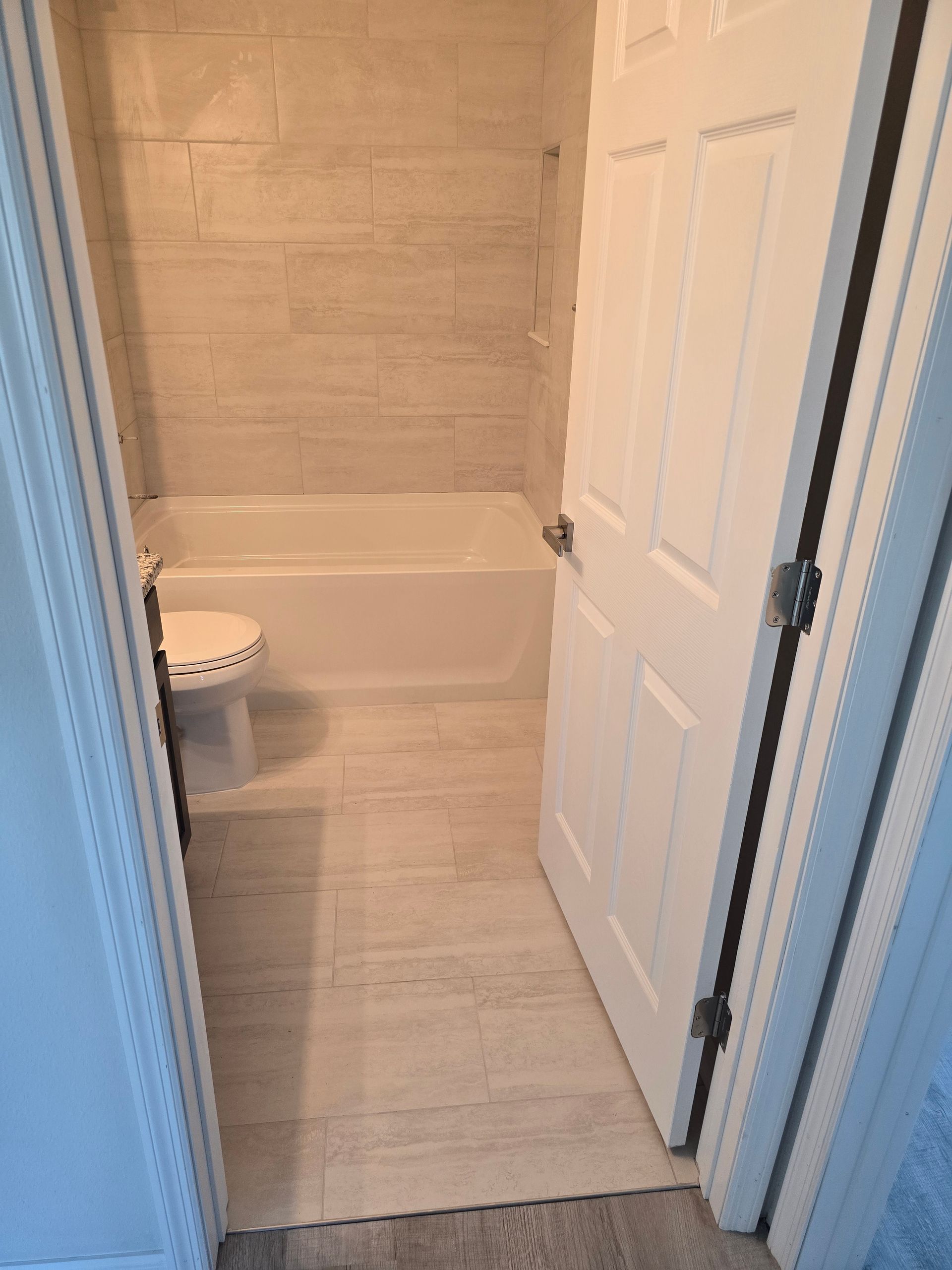 Small bathroom with white tub, beige tiled walls, and an open door.