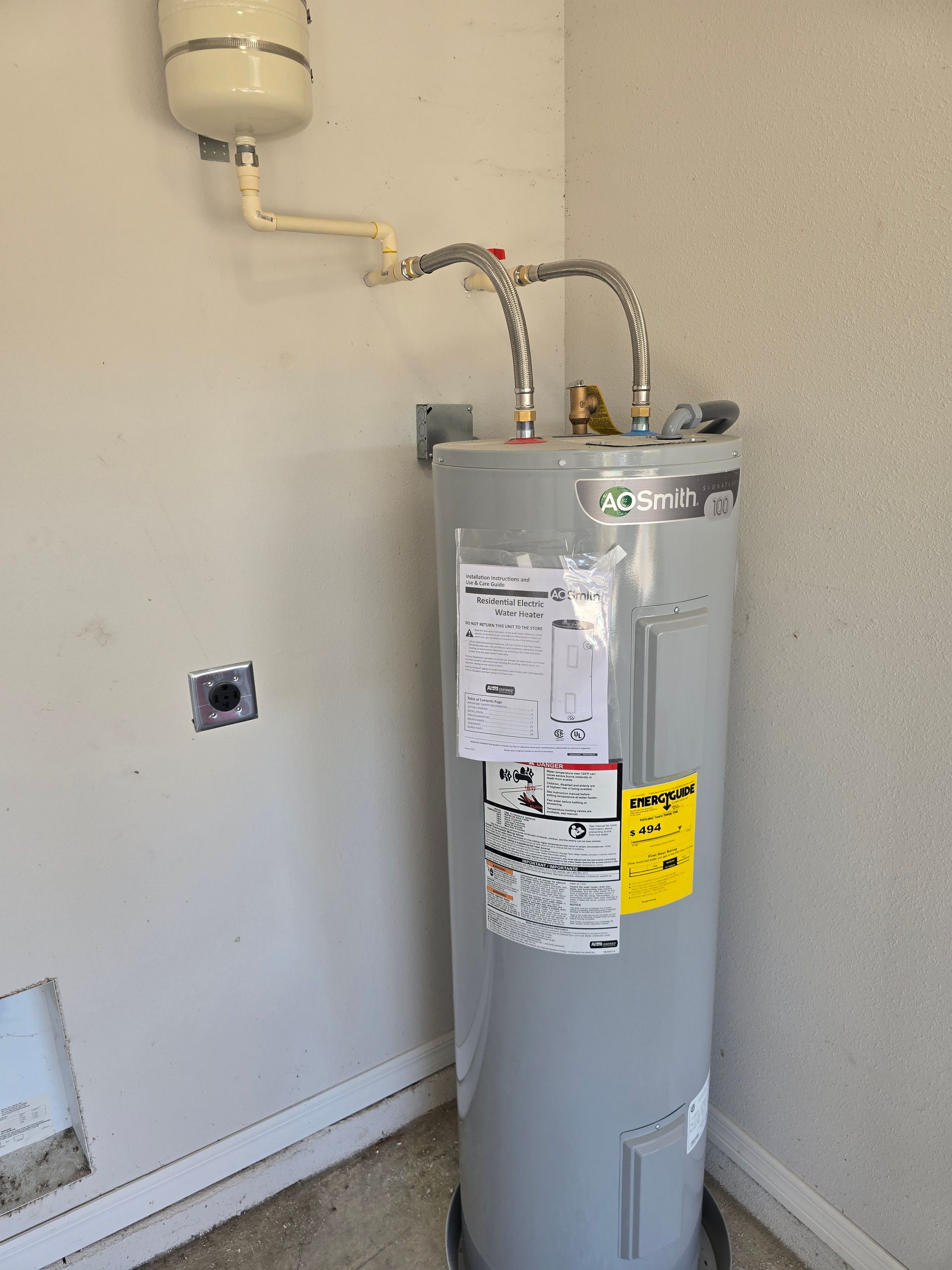 Gray water heater with pipes and labels in a utility room corner