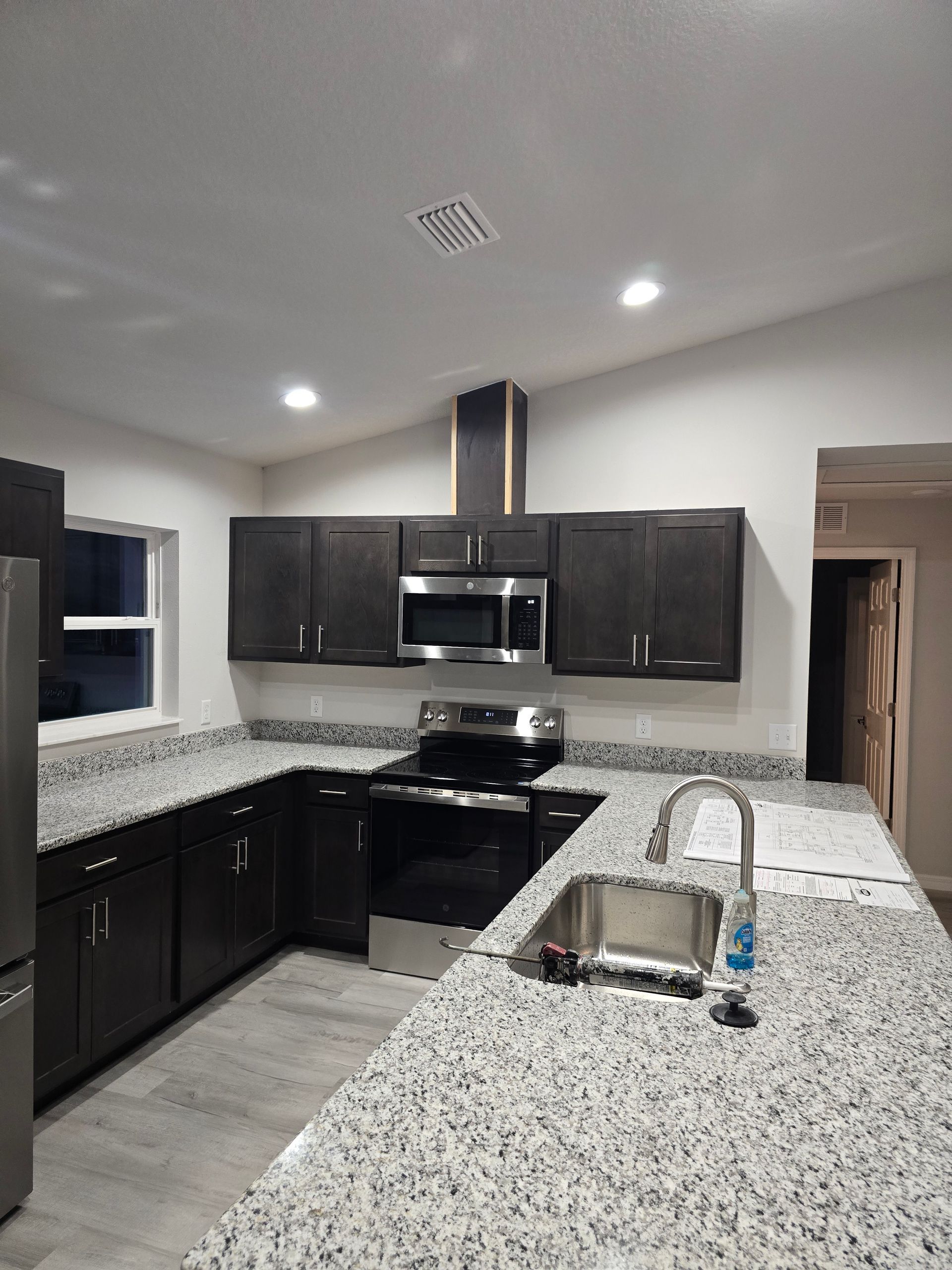 Modern kitchen with dark cabinets, speckled countertops, stainless appliances, and recessed ceiling lights