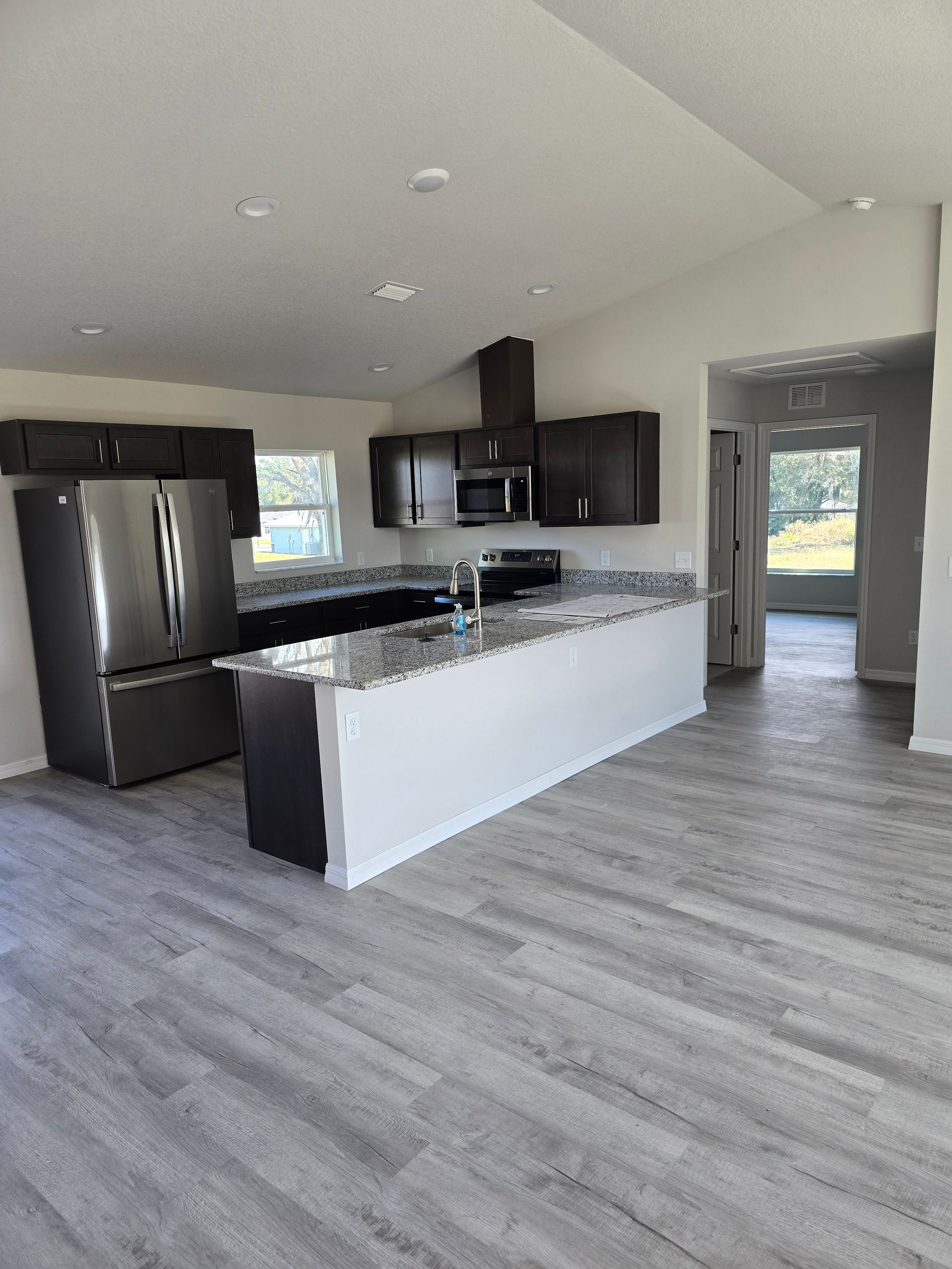 Modern kitchen with black appliances, white cabinets, gray countertops, and wood-look flooring.