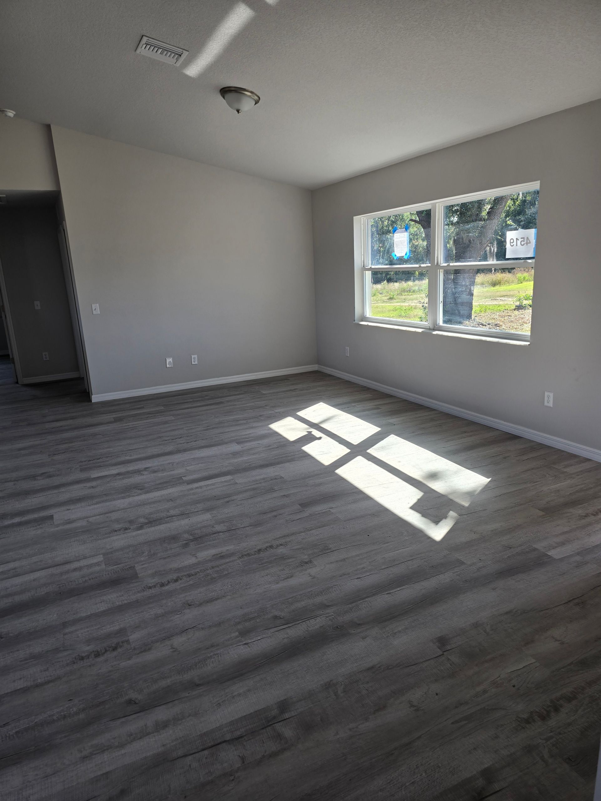 Empty room with gray walls, dark carpet, and sunlight streaming through a window.