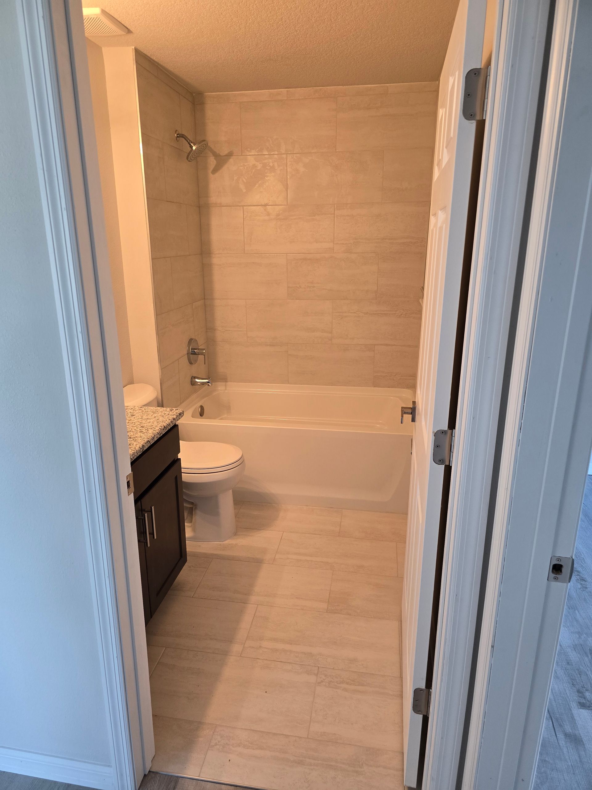 View into a modern tiled bathroom with a bathtub, toilet, and vanity.
