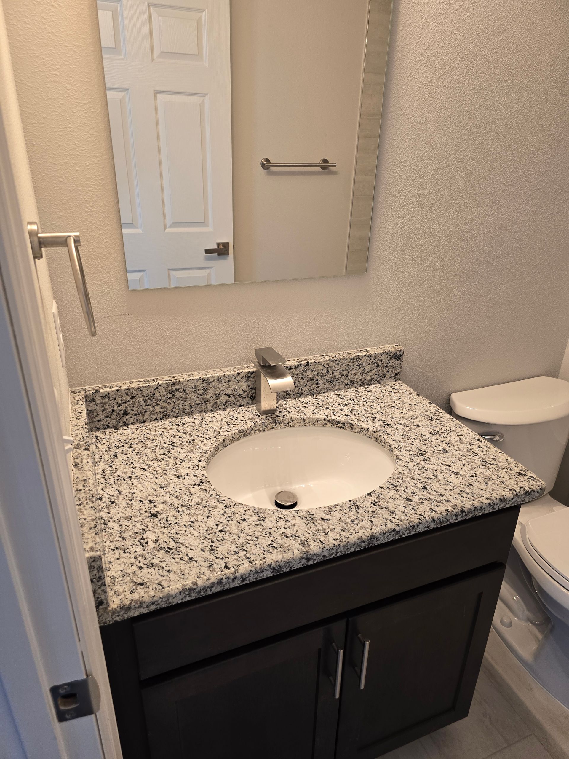 Bathroom vanity with speckled countertop, round sink, mirror, and towel bar.