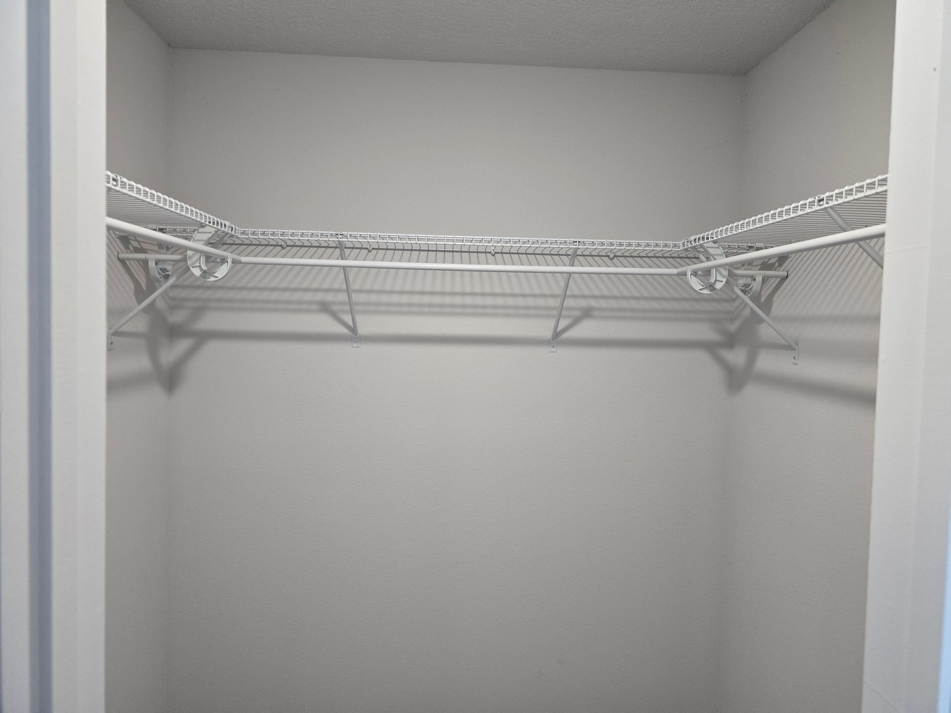 Empty closet with white wire shelves and hanging rods on two sides