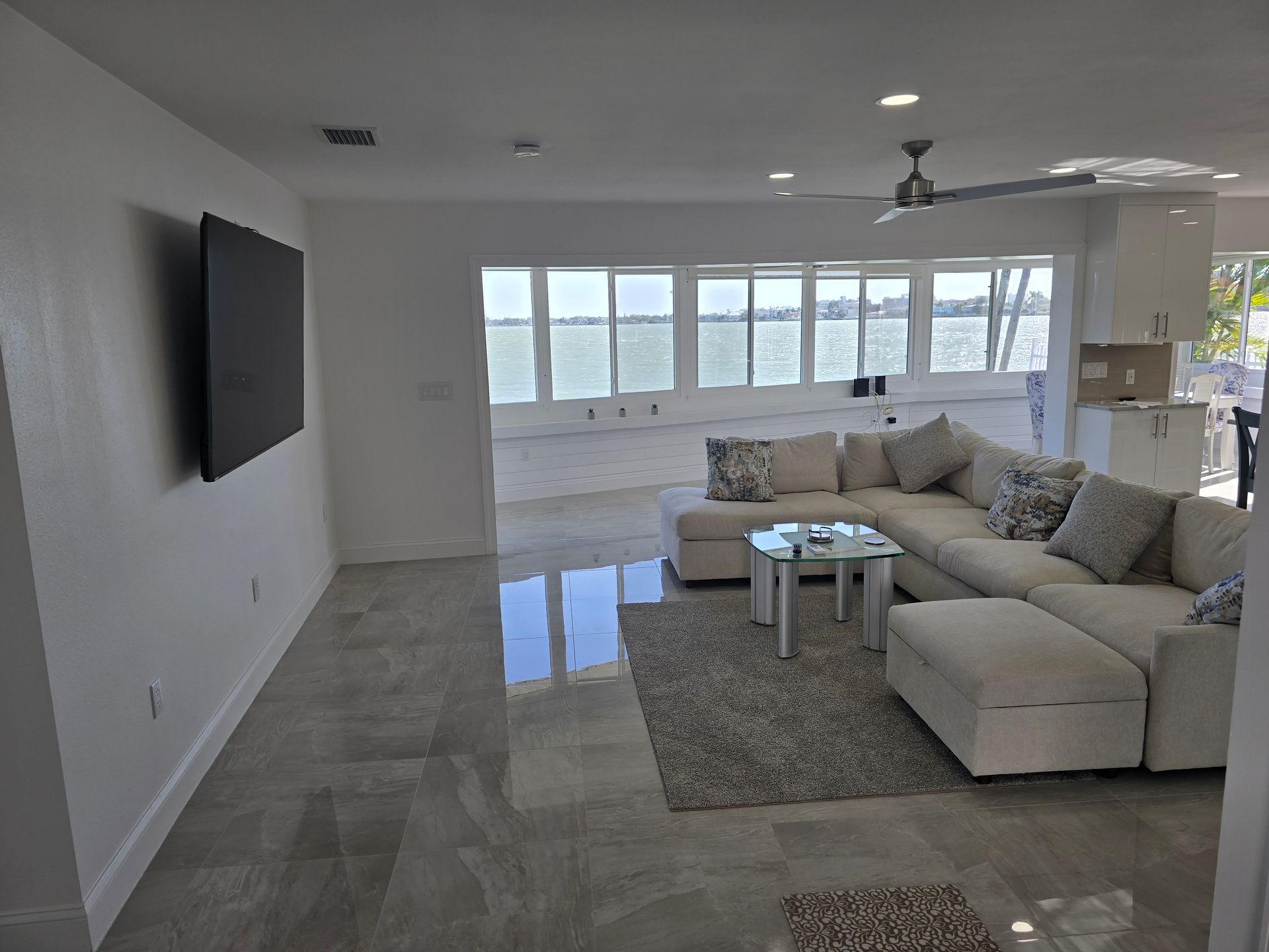 Modern living room with sectional sofa, wall-mounted TV, and large windows overlooking water.