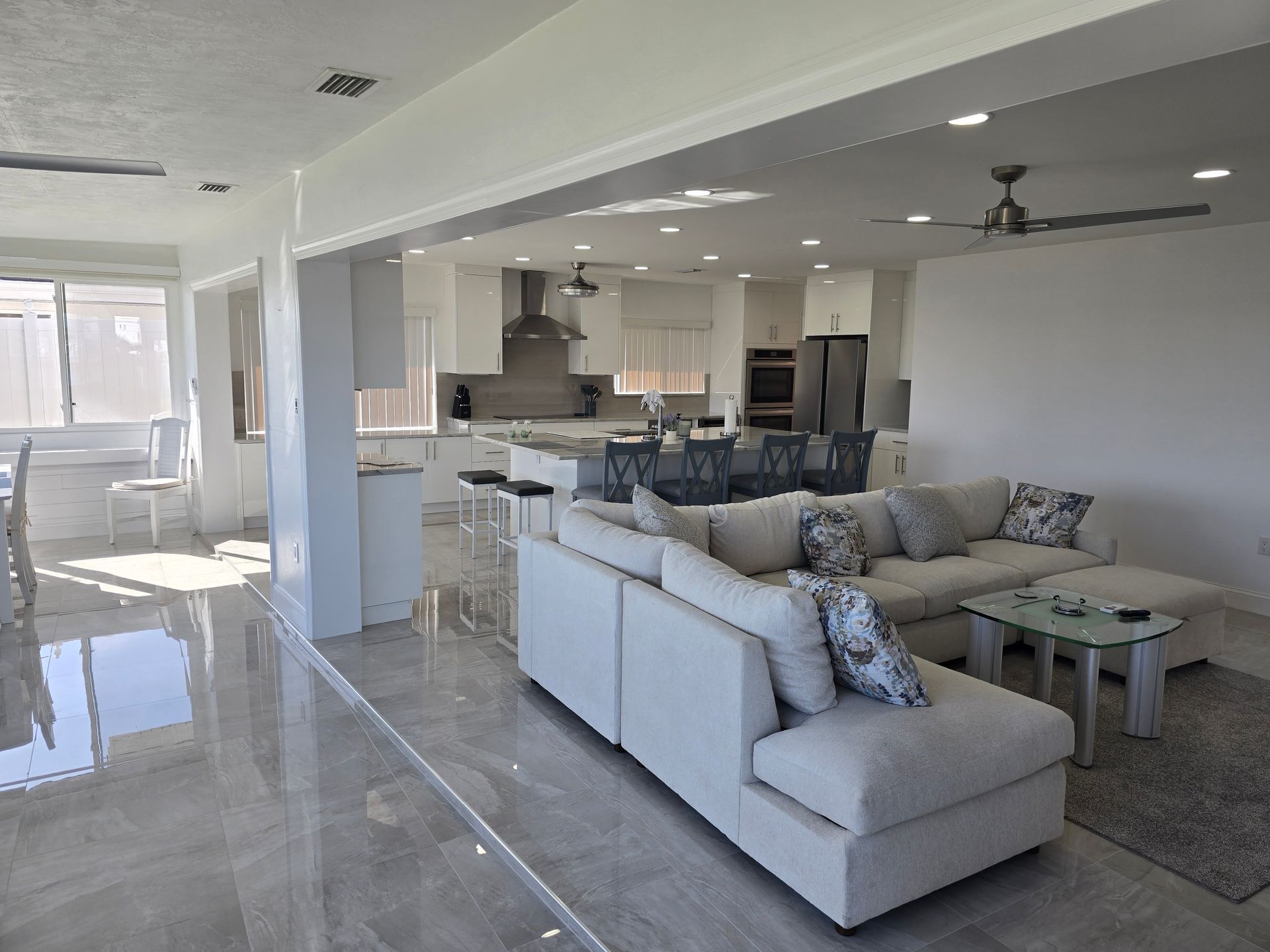 Bright open-plan living room with white sofas, rug, and kitchen in the background