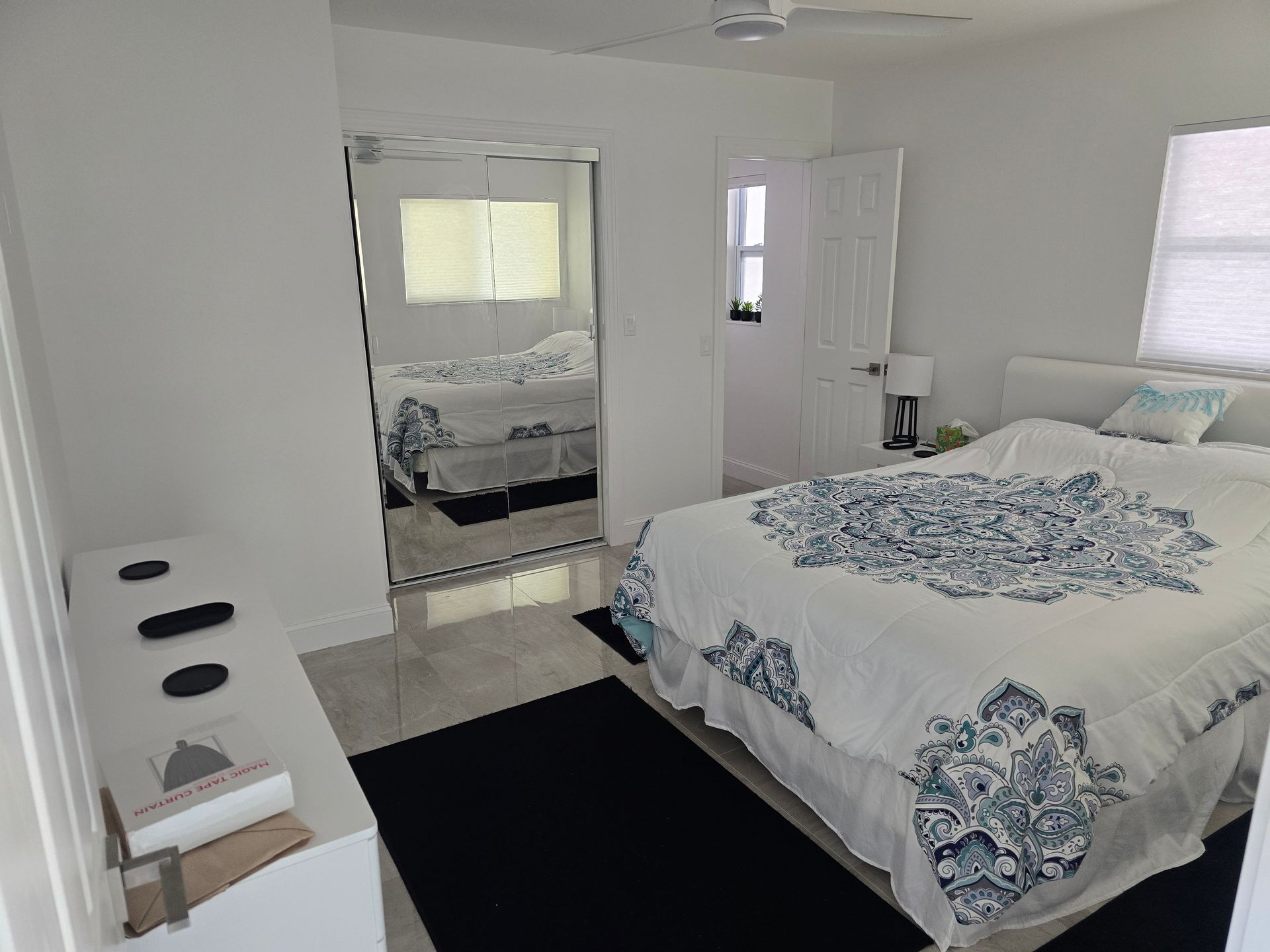 Bright bedroom with a bed, wall mirror, and black rug on a white floor