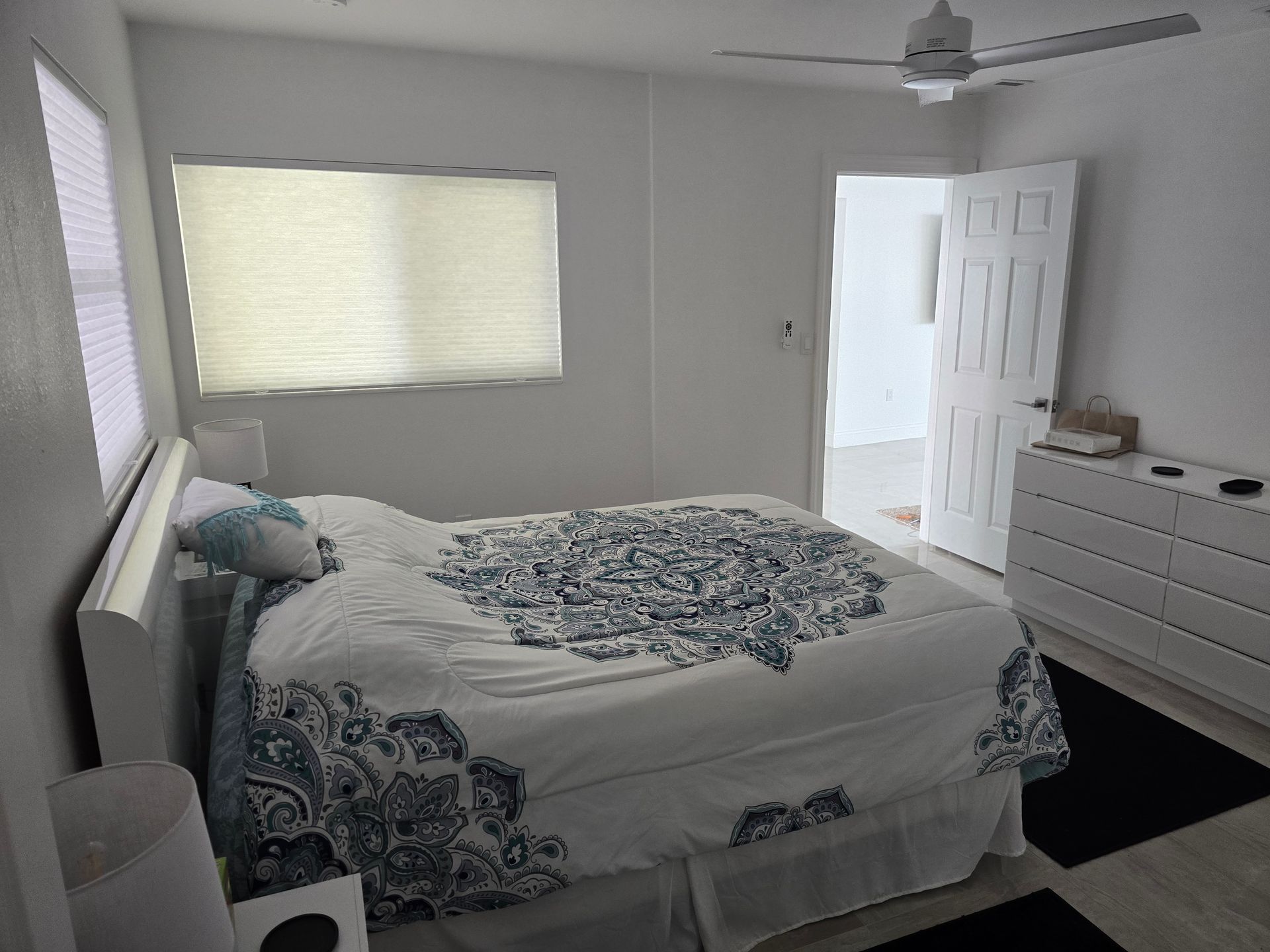 Bright bedroom with a bed, dresser, window, ceiling fan, and open door.