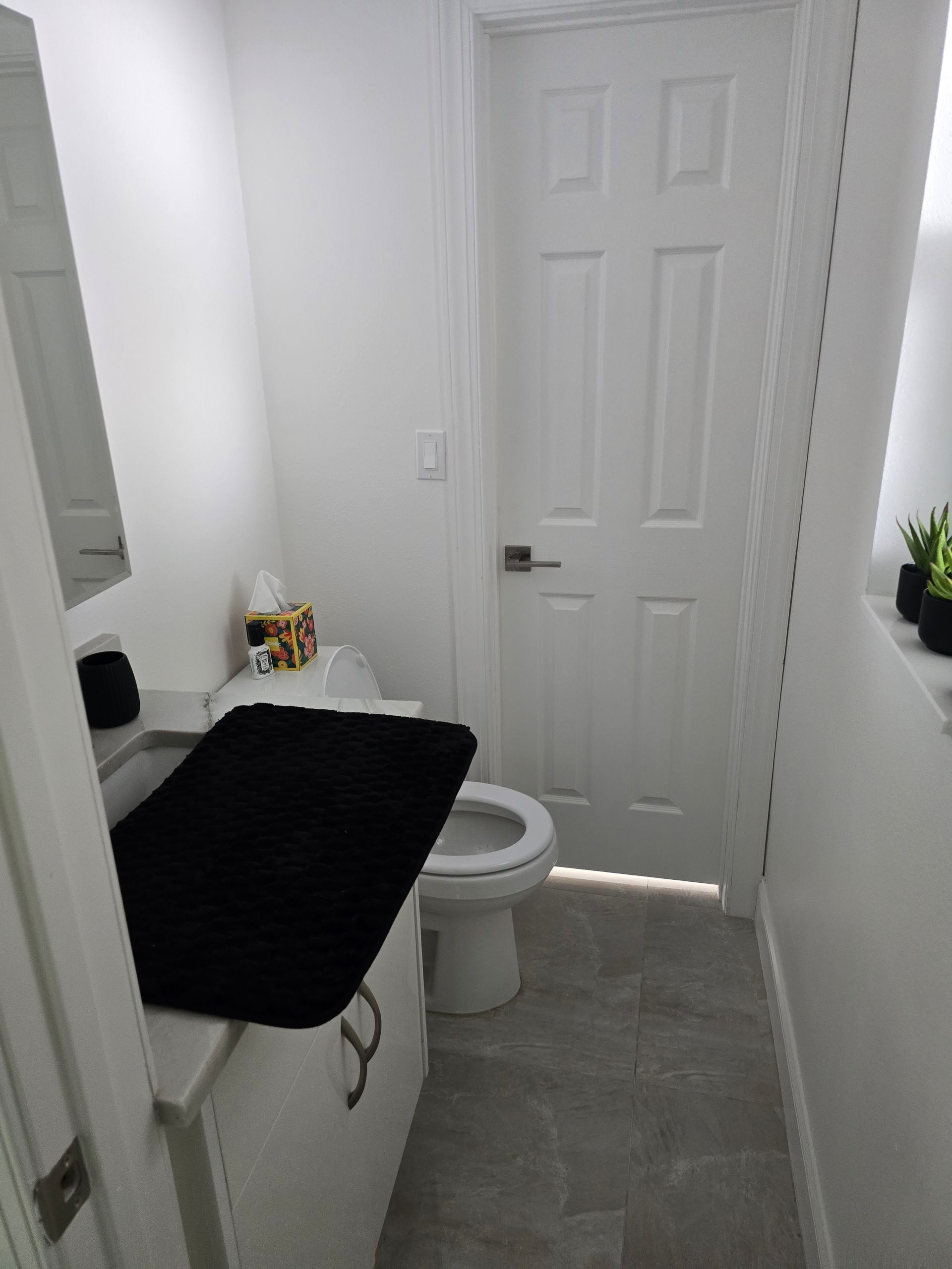 Small bathroom with toilet, vanity, gray tile floor, and closed white door.
