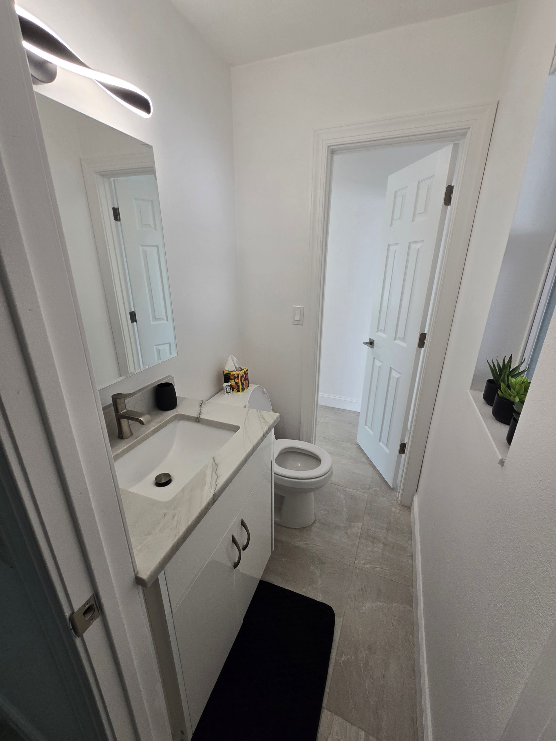 Narrow white bathroom with vanity, mirror, toilet, and shower curtain