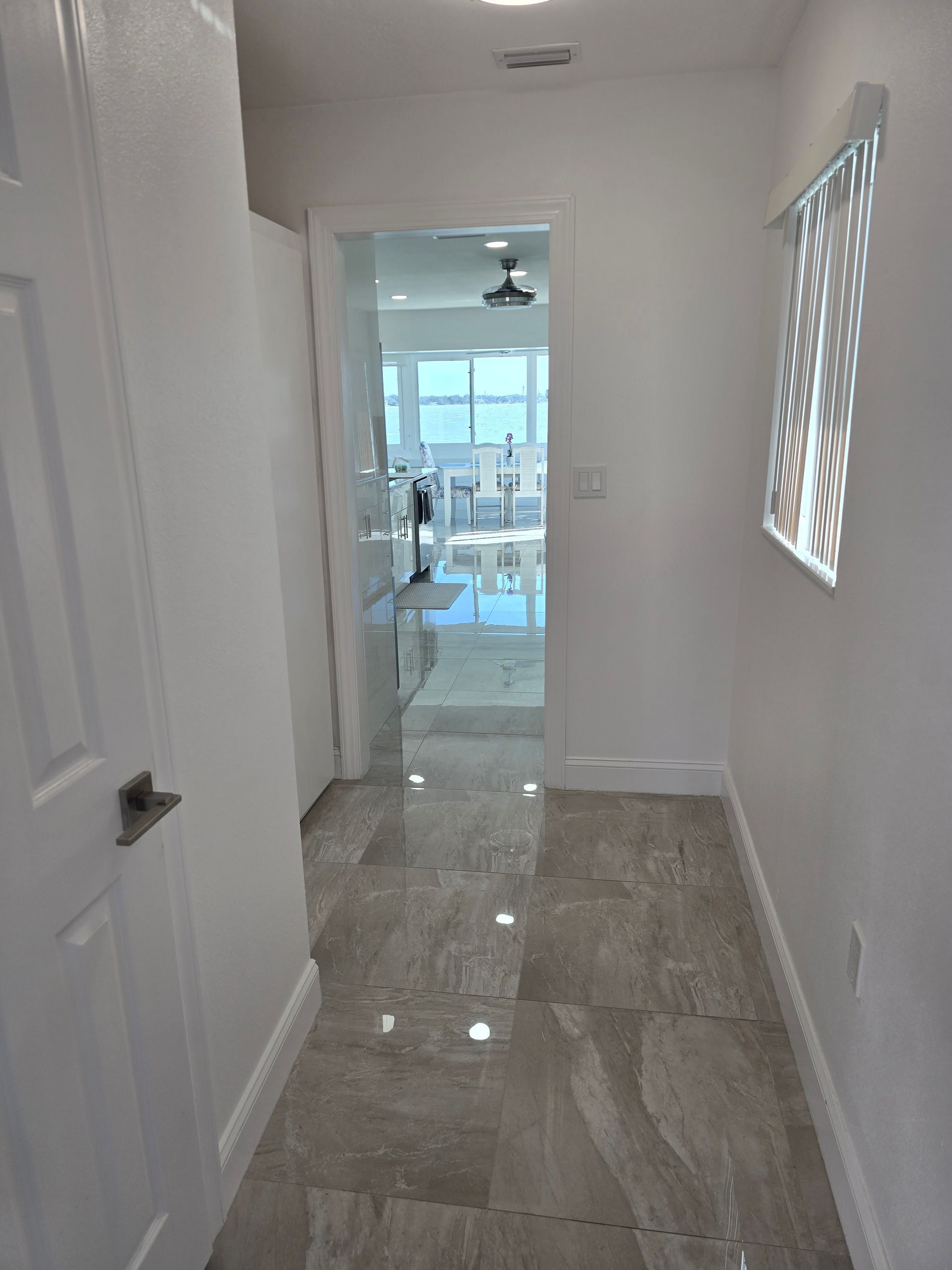 Narrow white hallway with glossy tile floor leading to a bright room with ocean views.