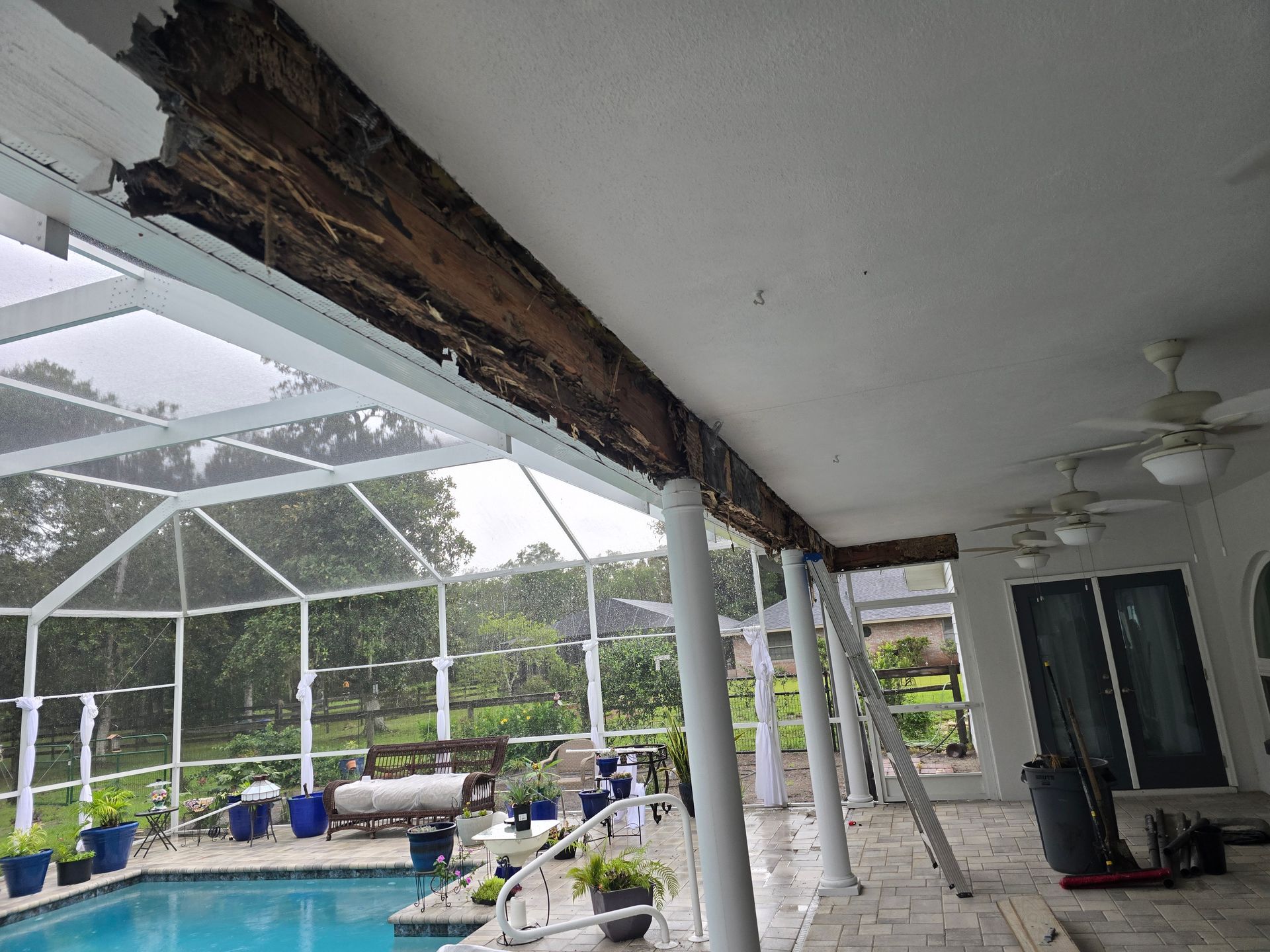 Covered patio with white columns, exposed wooden beams, and a screened pool area beyond