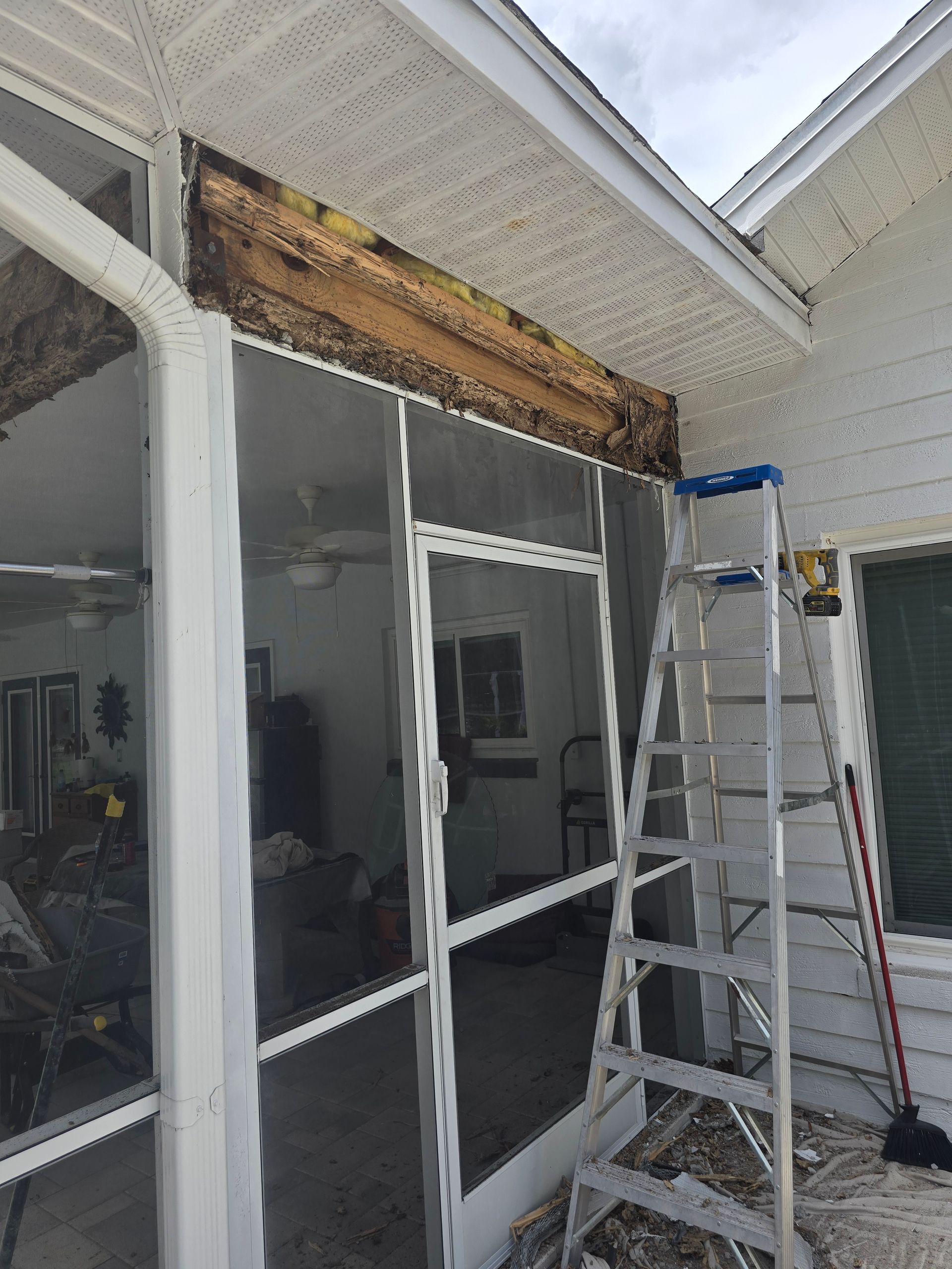 Damaged entryway soffit being repaired, with ladder and tools beside a screened porch