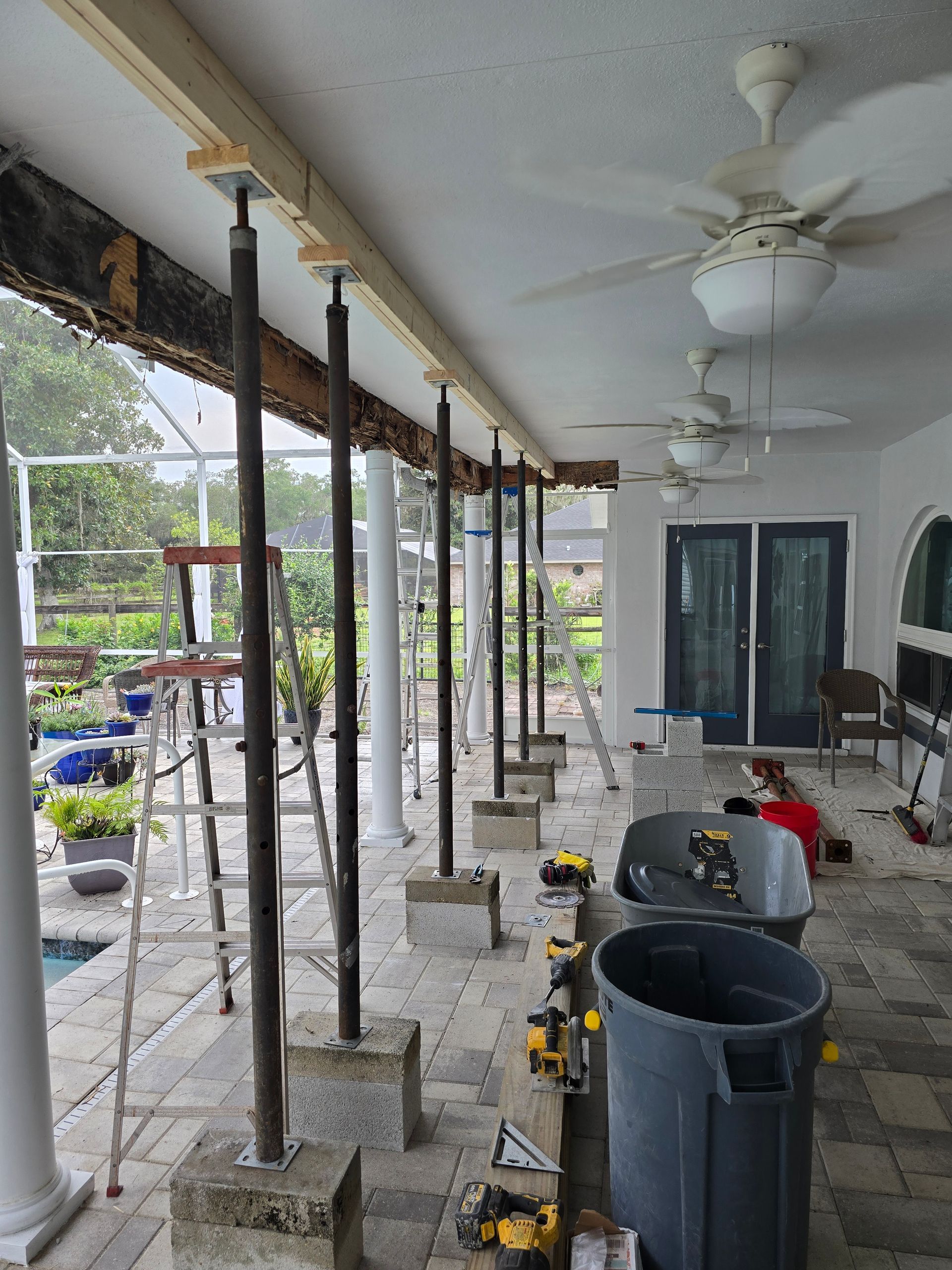 Covered porch under construction with white columns, tools, buckets, and ceiling fans